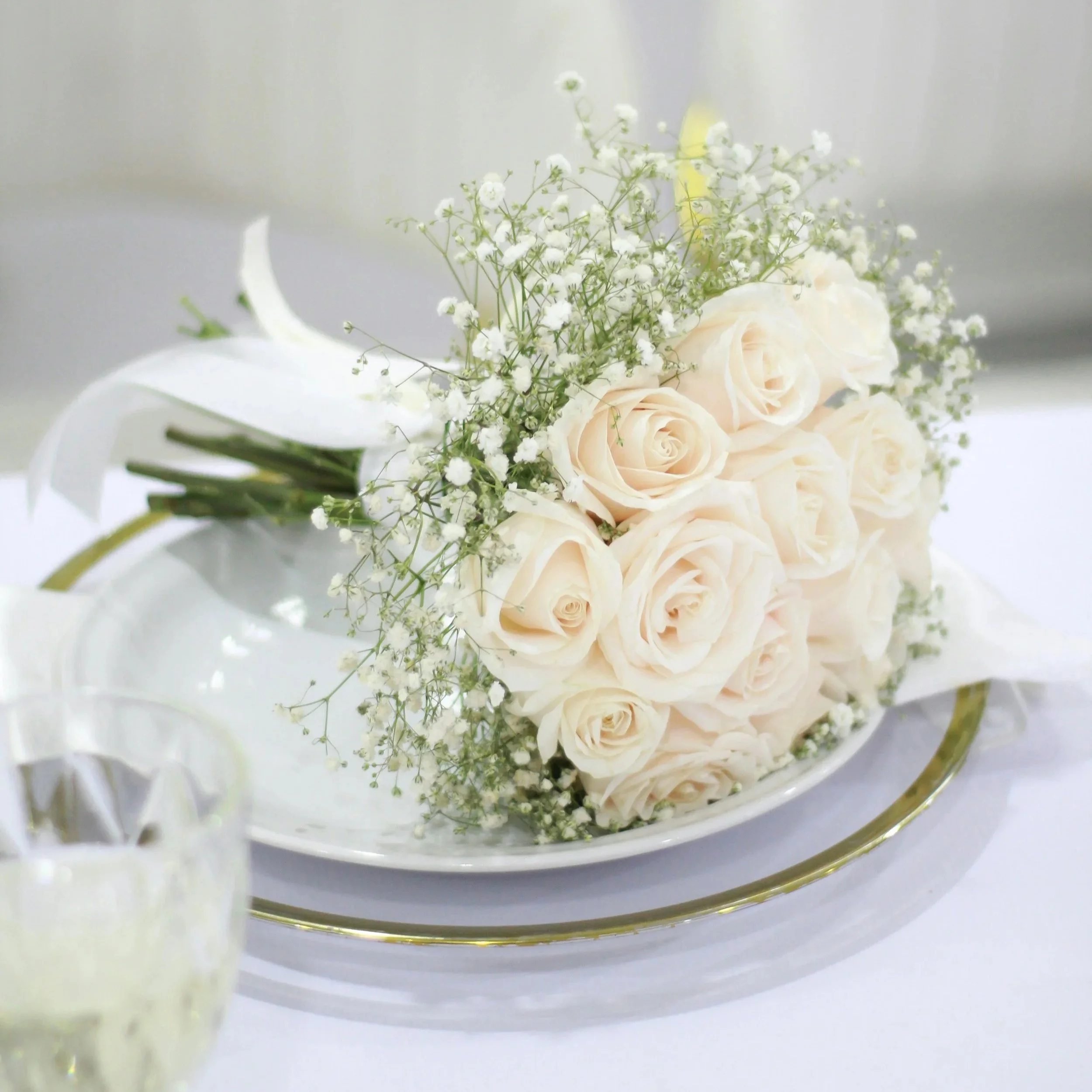 Blumengesteck mit weißen Rosen und Schleierkraut in einer weißen Vase auf einem silbernen Tablett.