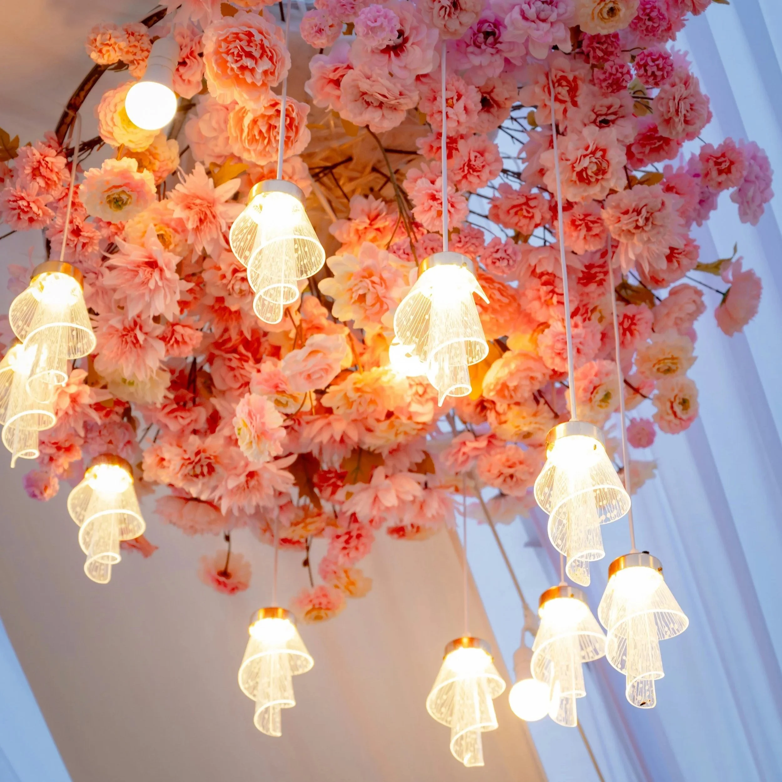 Hintergrund mit rosa Blumen und mehreren weißen Lampen in Form von Blütenblättern, die nach unten gerichtet sind.