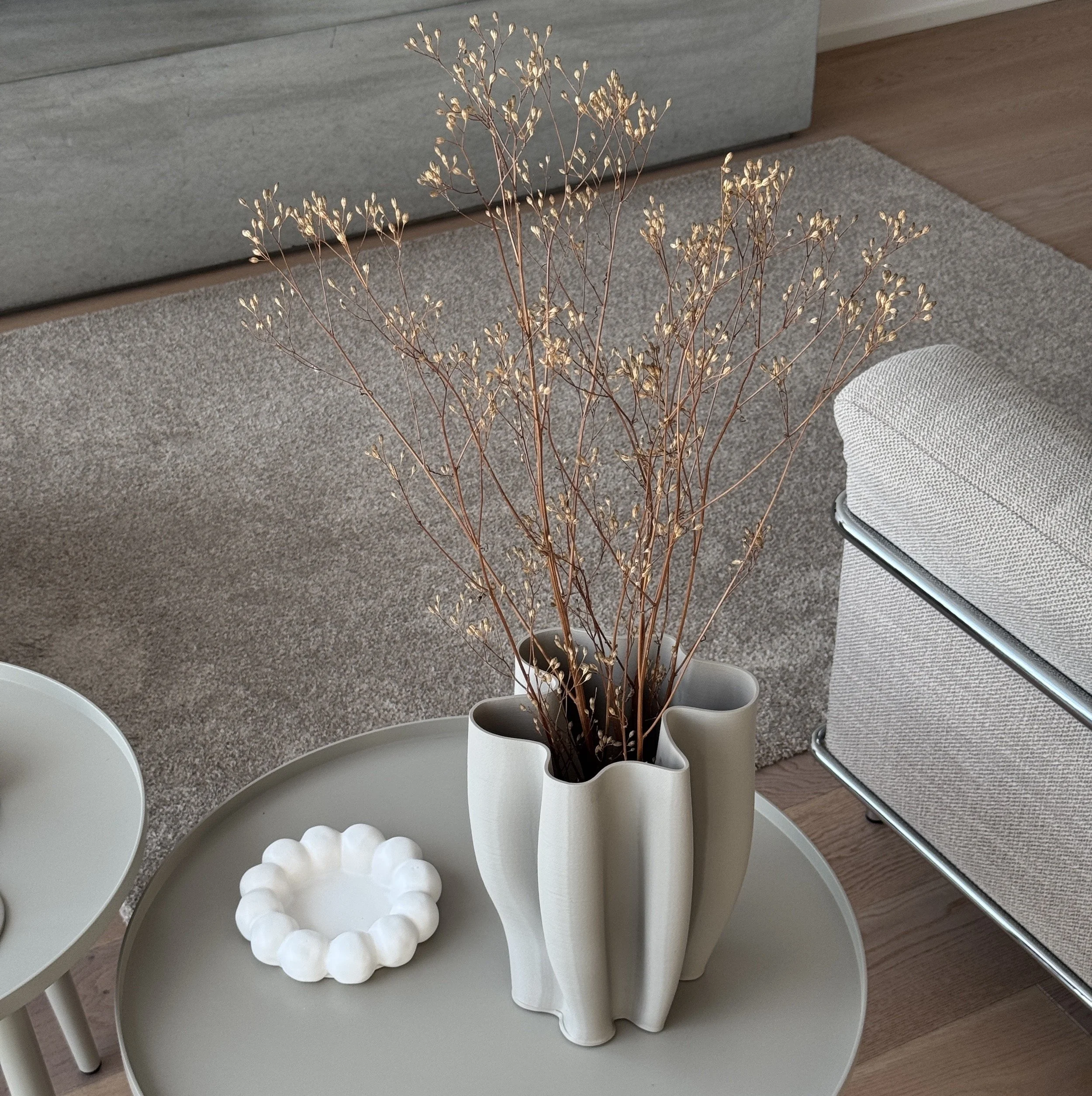 Bauchige weiße Vase mit Trockenblumen auf einem runden weißen Tisch in einem modernen Einrichtungsraum.