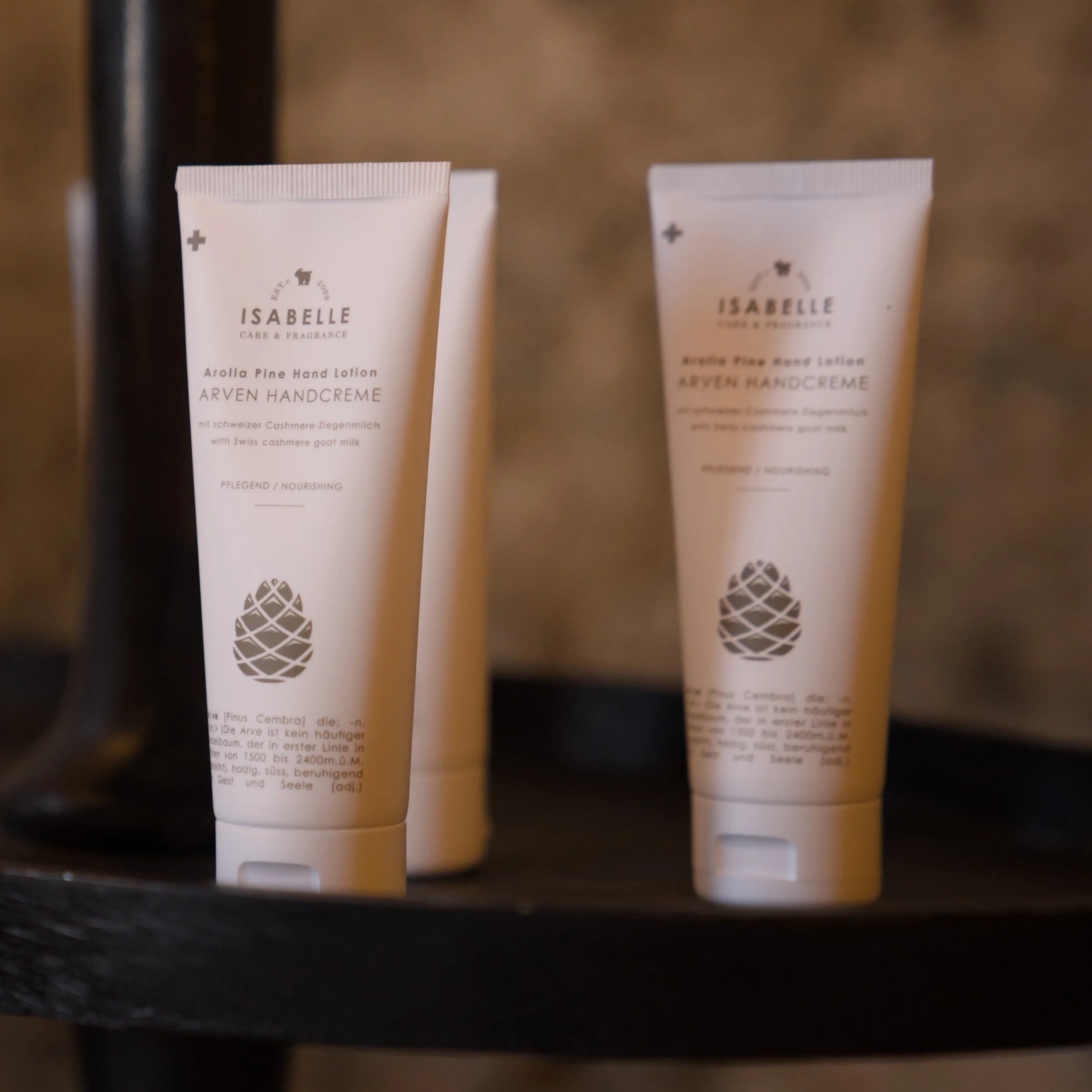 Zwei weiße Tuben auf einem schwarzen Regal. Die Tuben sind mit schwarzer Schrift und einem Symbol eines Maulwurfs bedruckt. Der Text zeigt, dass es sich um eine Handcreme handelt, die mit Schweizer Ziegenmilch hergestellt ist.