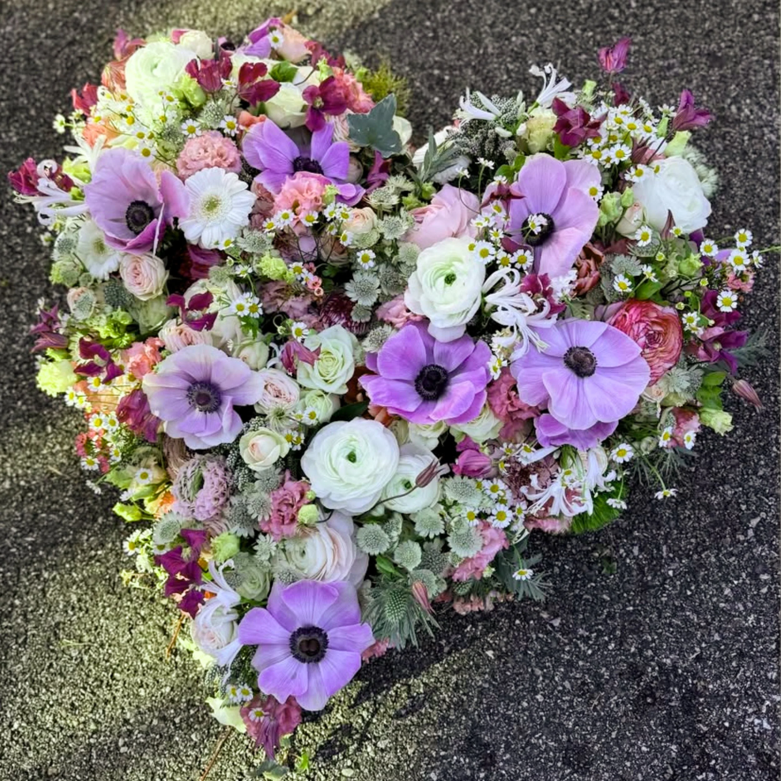 Blumengruß mit lilafarbenen, weißen und pinken Blumen auf dunklem Boden.