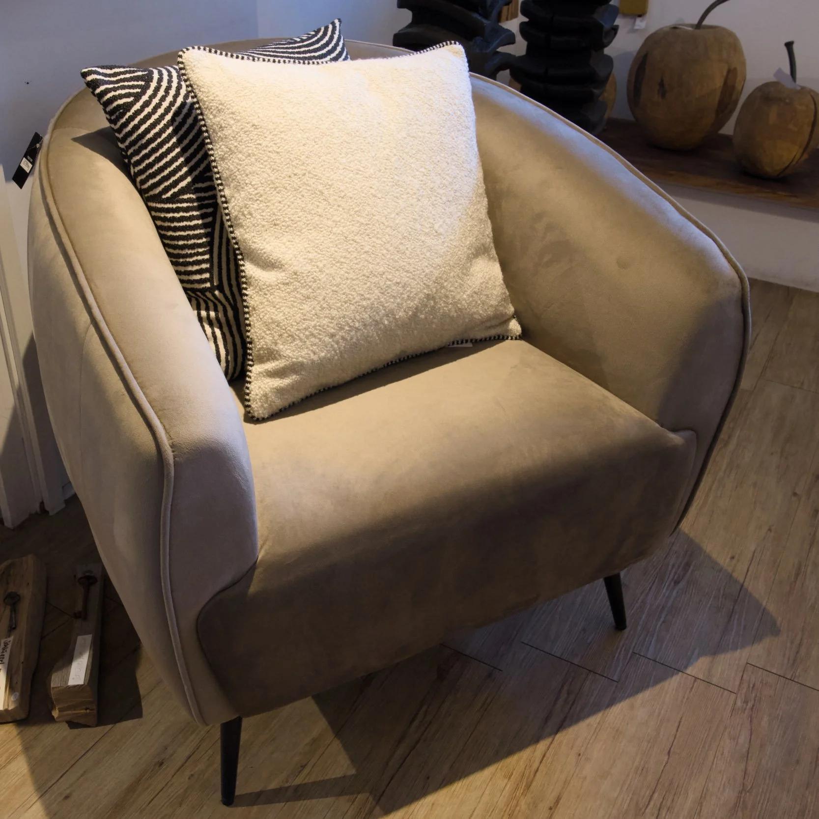 Ein beiger, gepolsterter Sessel mit schwarzen Beinen, dekoriert mit zwei schwarzen und weißen Kissen sowie einem weißen Kissen