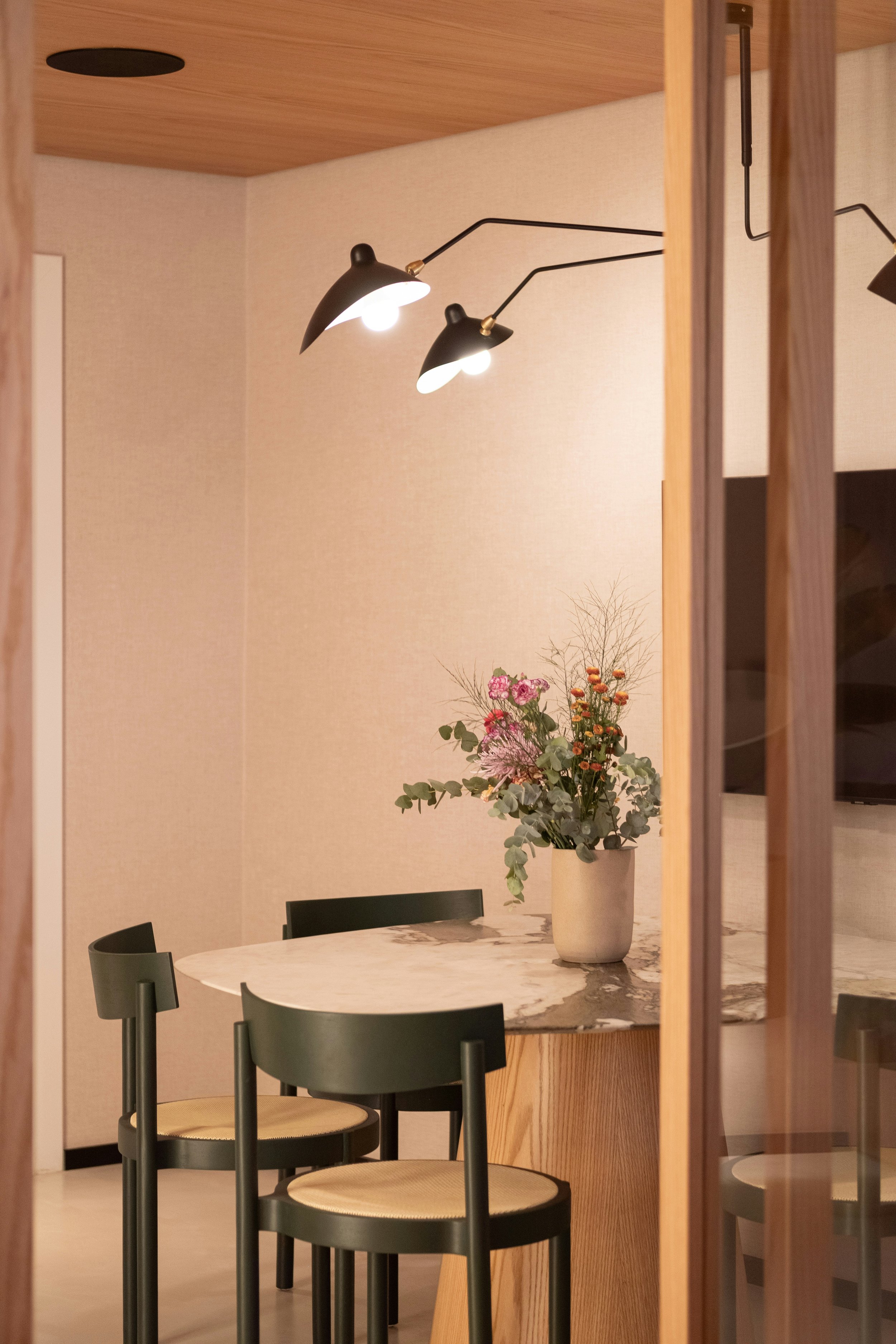 Ein Esszimmer mit einem runden Marmor-Tisch, schwarzen Stühlen, einer Vase mit Blumen und einer Wandlampe.