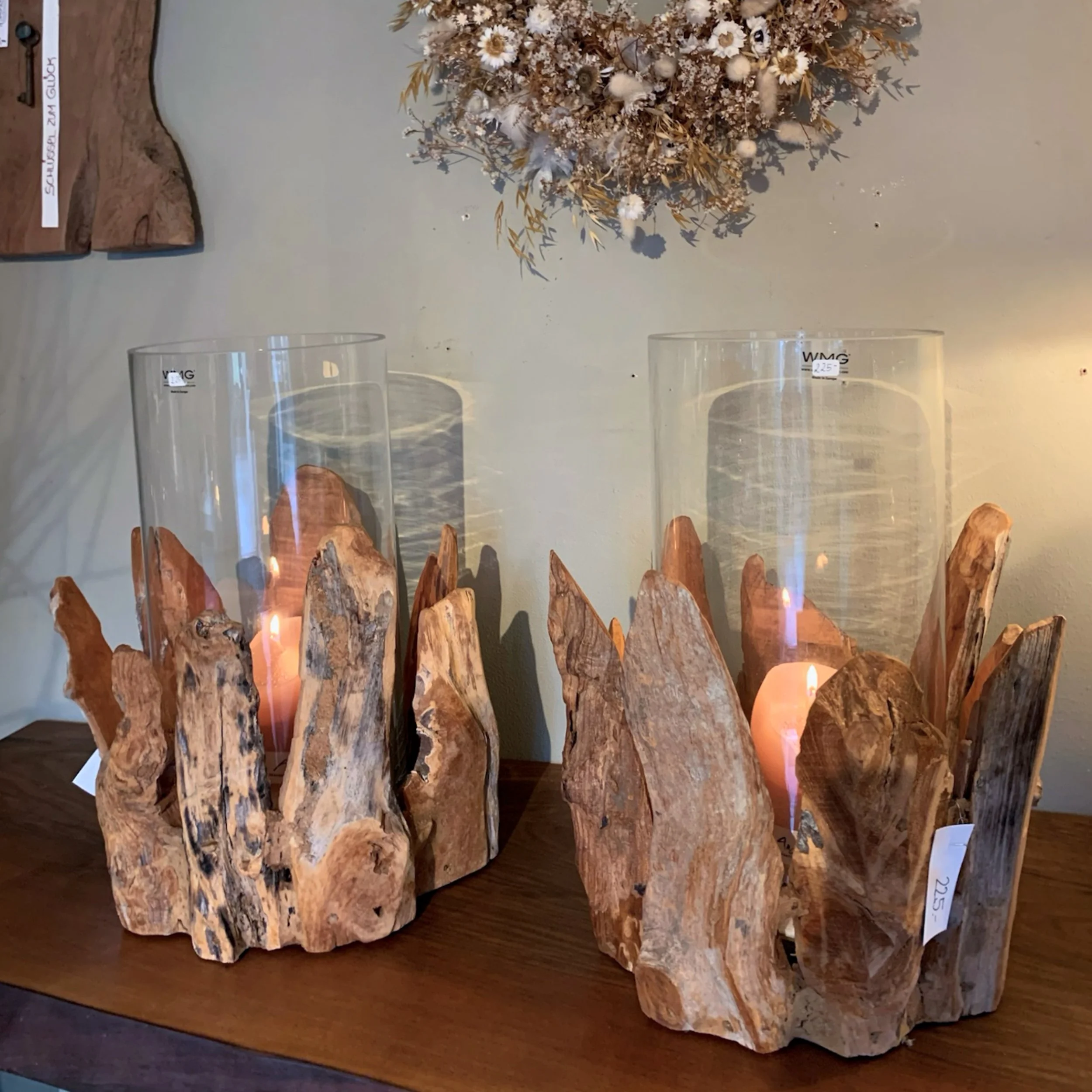 Holzskulptur mit Kerzen und Trockenblumen auf einem Tisch.