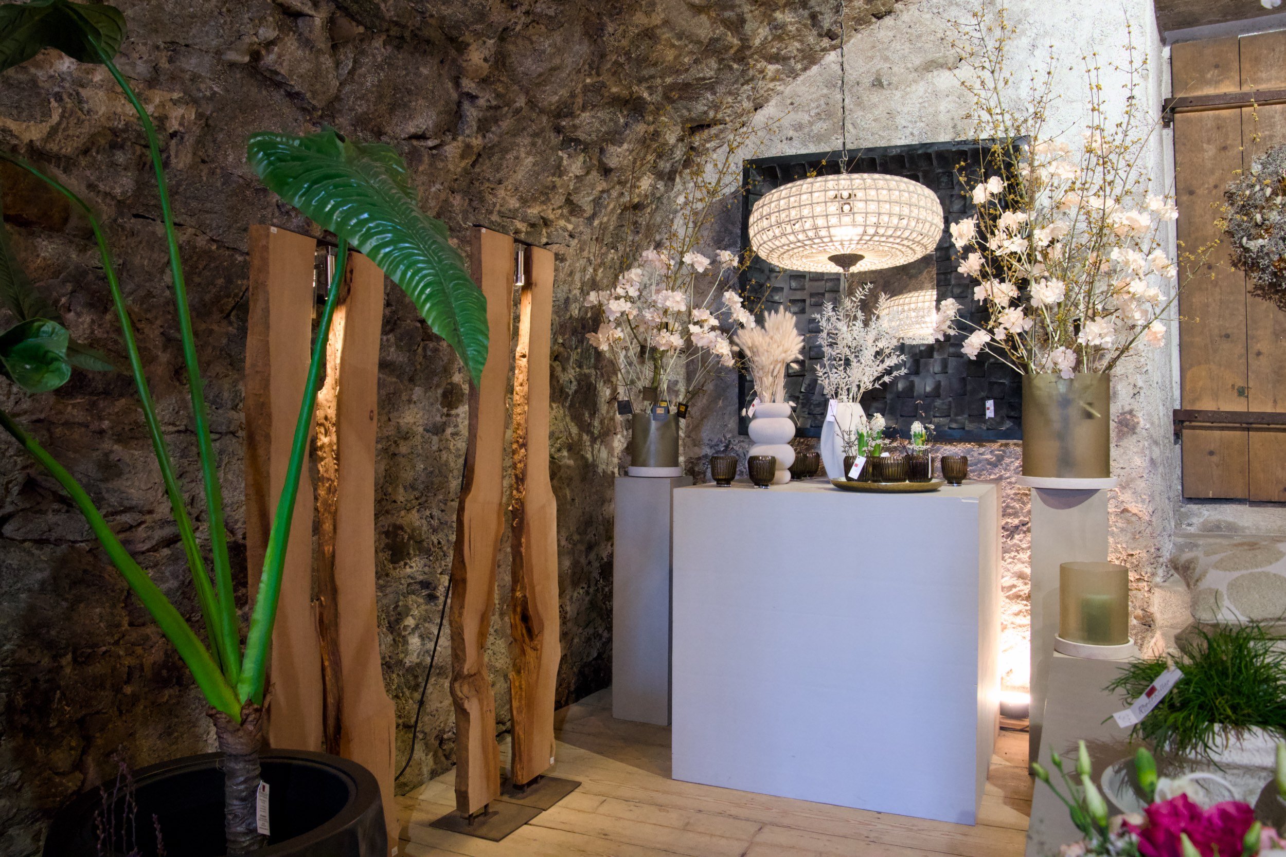 Inneneinrichtung mit Pflanzen, einer Deckenlampe und Blumenvasen in einem Raum mit Steinfundamenten.