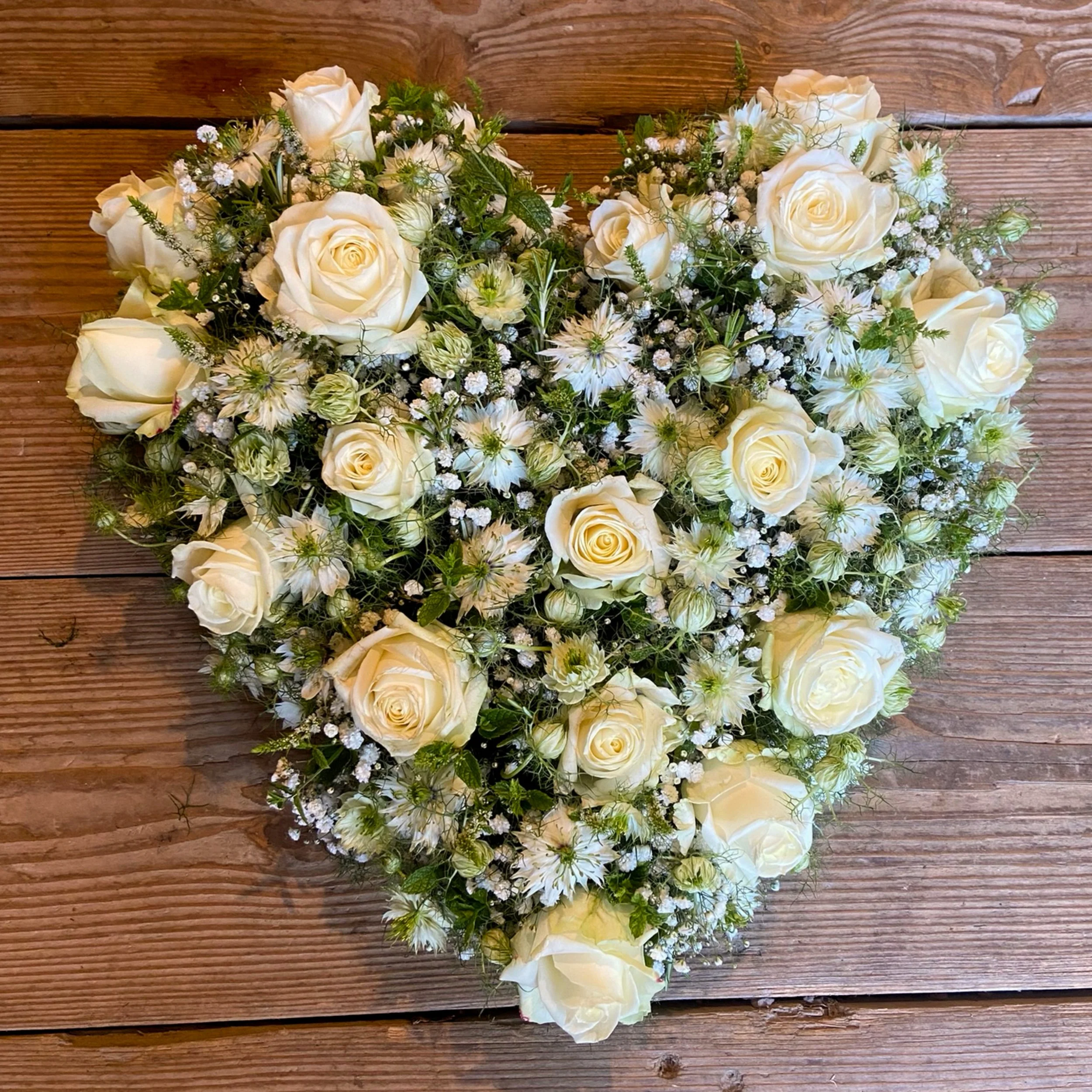 Eine weiße Blumenkrone mit Rosen, kleinen weißen und grünen Blumen, auf einem Holztisch