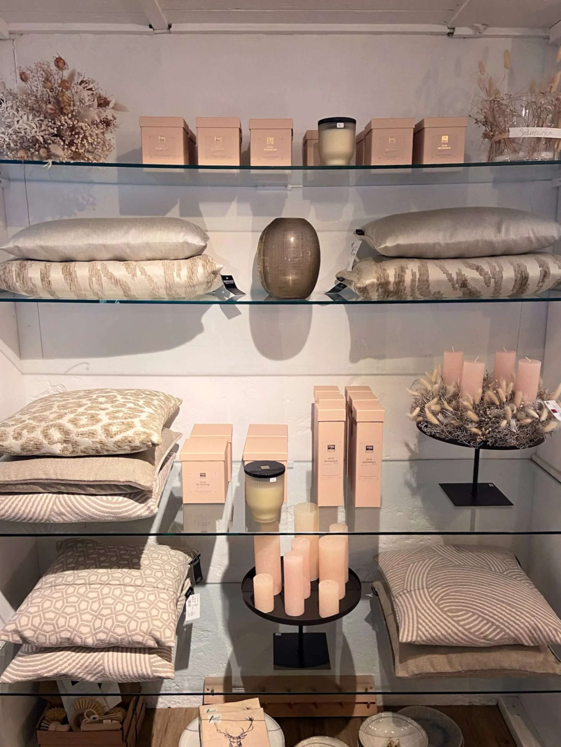 Dekorative Kissen in neutralen Farben, Vasen und Deko-Elemente, trockene Blumen und Kerzen auf einem Regal, alles in einem eleganten, neutralen Farbthema.