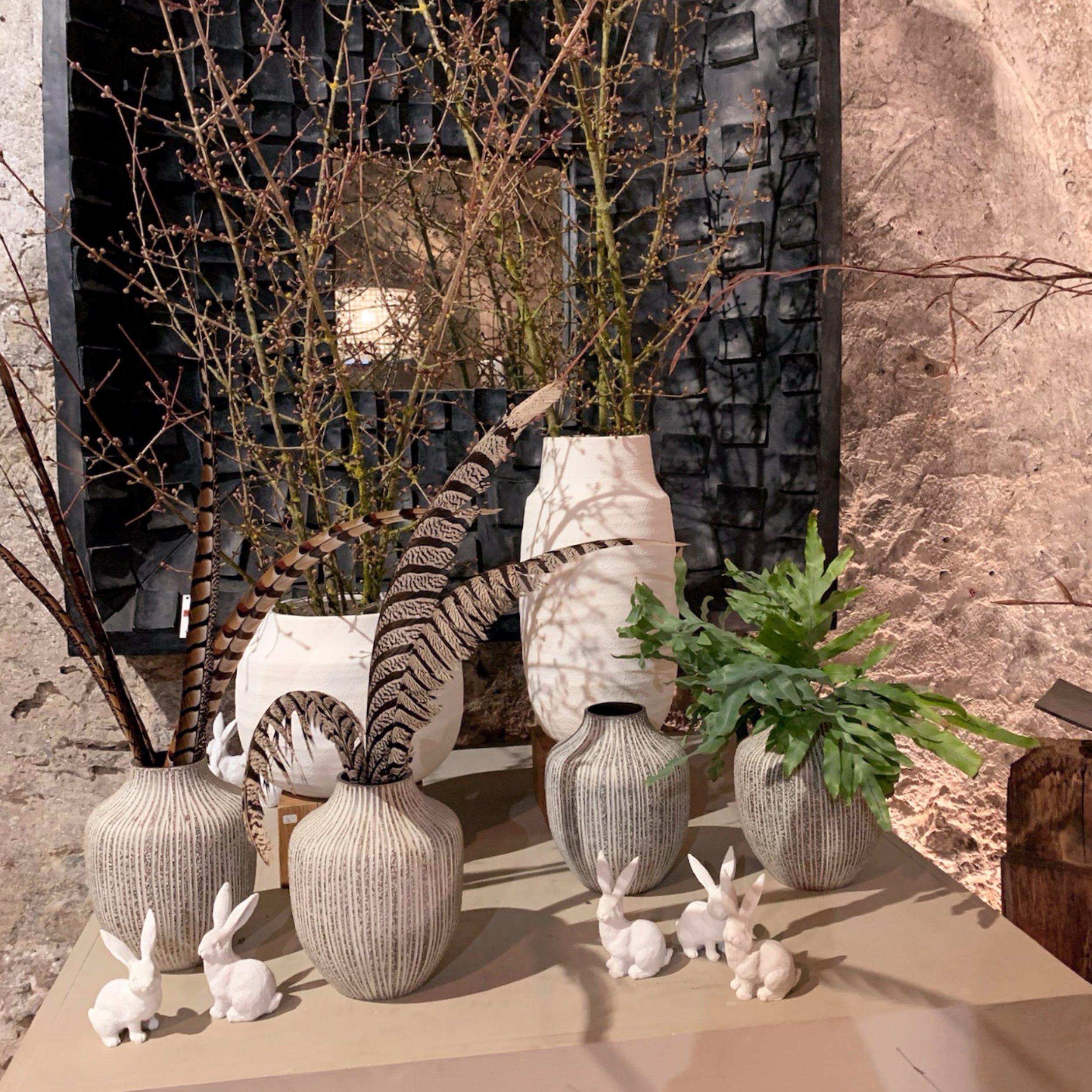 Dekorative Vasen mit Pflanzen und Blumen, umgeben von weißen Vogelskulpturen, auf einem Tisch in einer Verkaufsstelle für Wohnaccessoires.