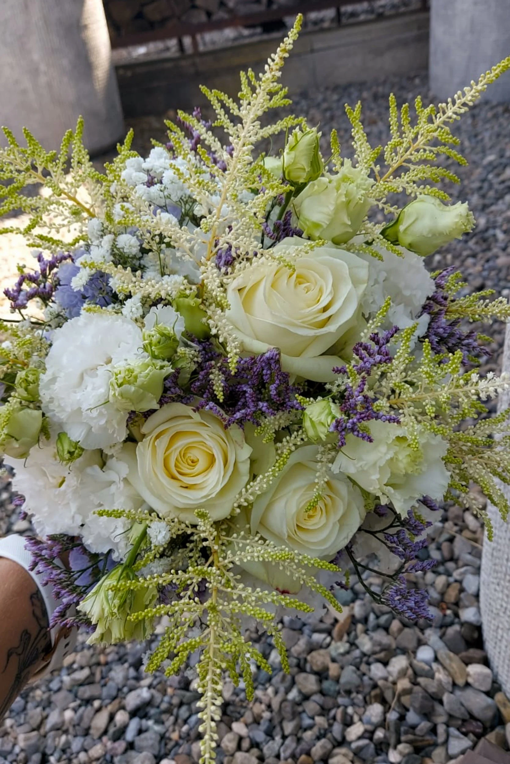 Blumenstrauß mit weißen Rosen, weißen Hortensien, lila Lavendel und weißen Stauden, auf einem Kopfsteinpflaster.