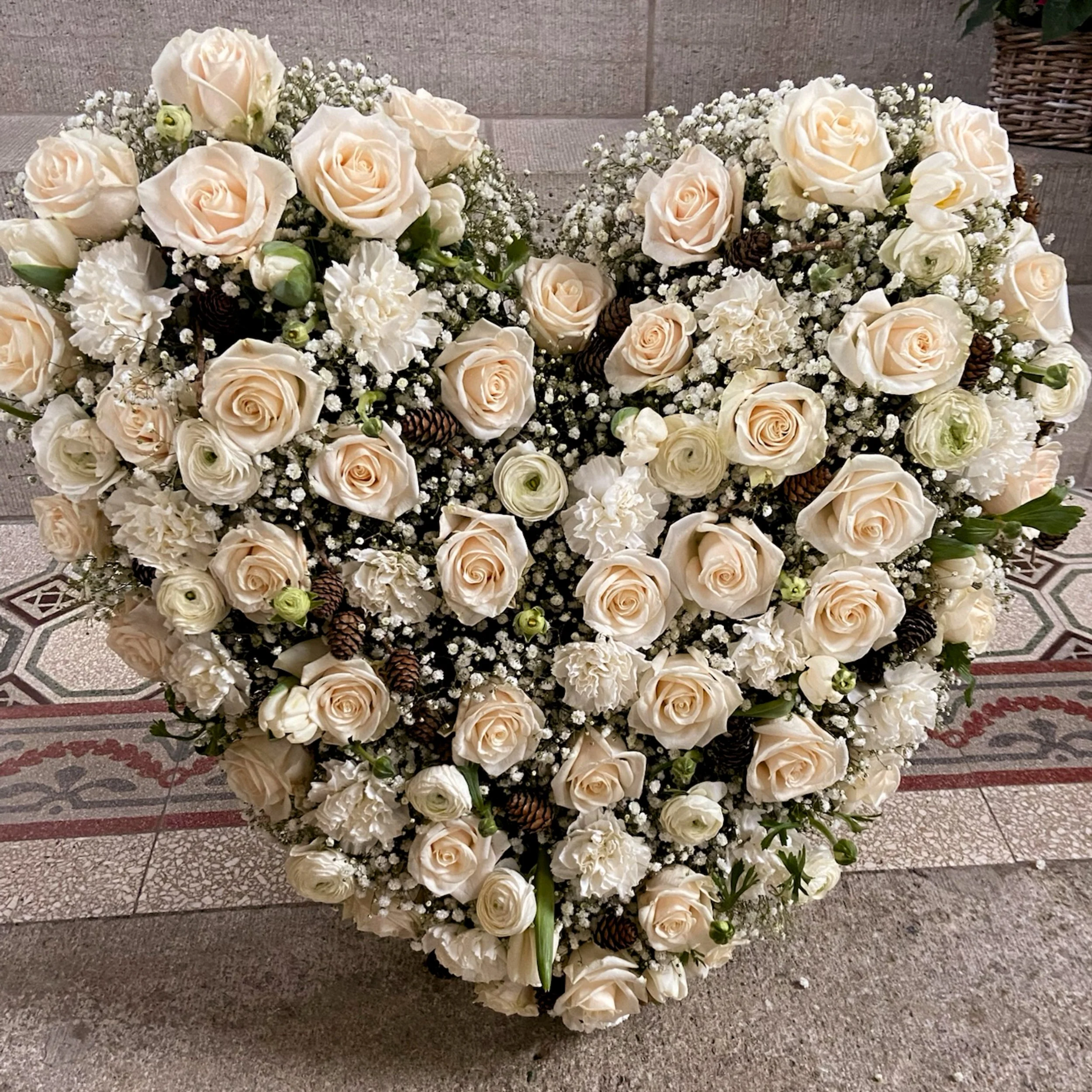 Ein Blumengesteck mit weißen und cremefarbenen Rosen, Bechern, Tannenzapfen und Baby's-b breath auf einem Steintreppenabsatz.