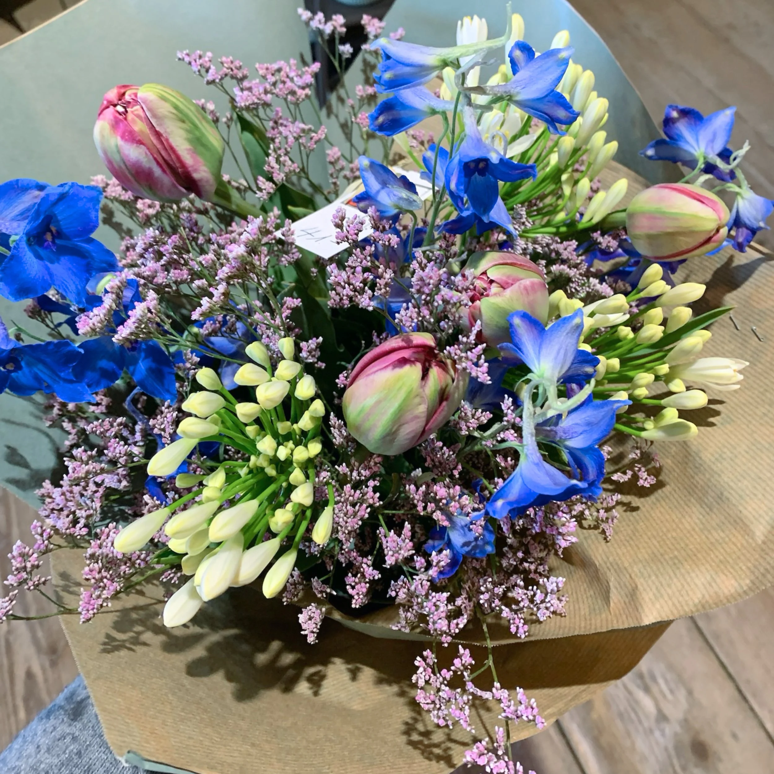 Blumenvase mit blauen, pinken, weißen und gelben Blumen auf einem Holztisch.