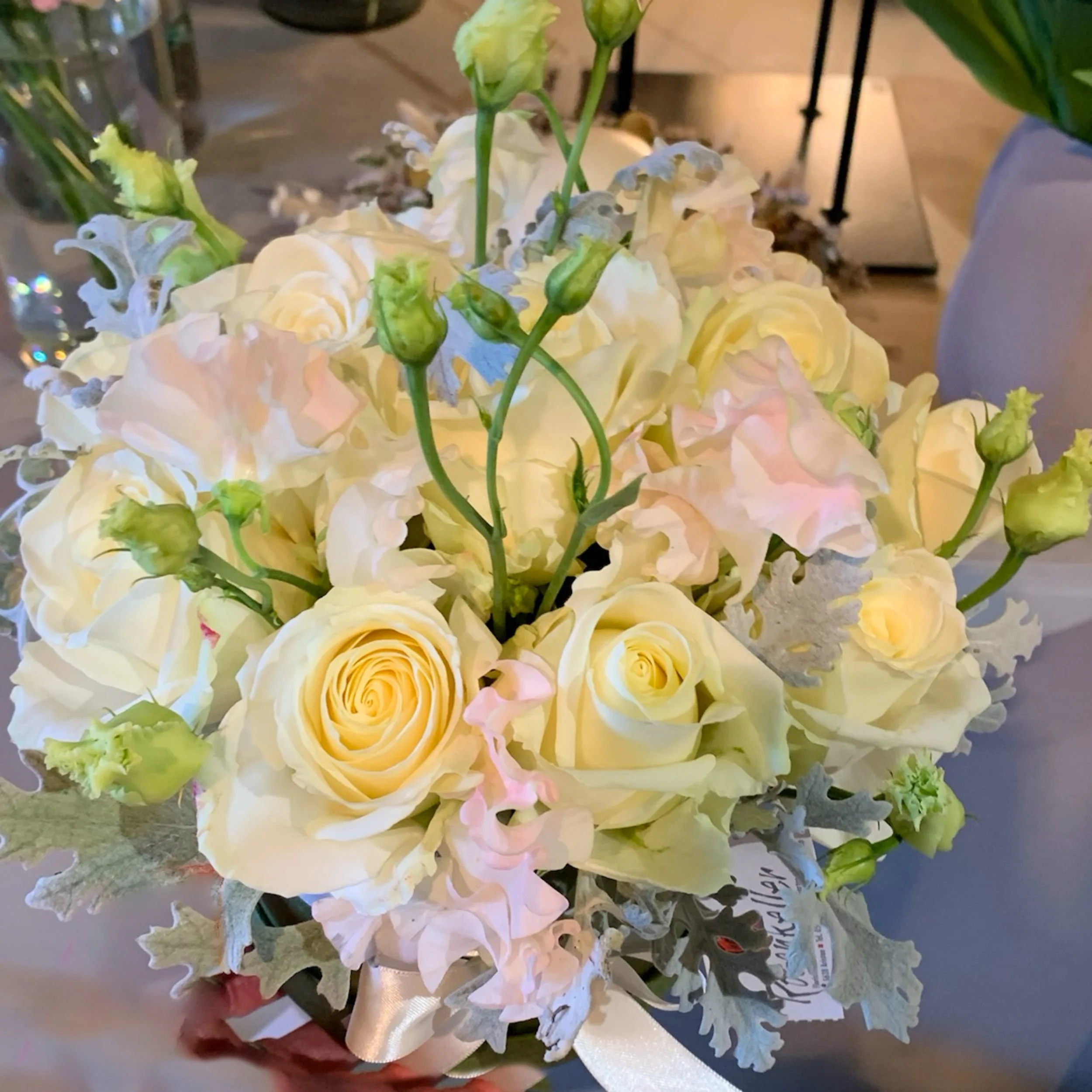 Ein Blumenstrauß mit weißen, blass rosa und gelben Rosen, grünen Knospen und zarten Blättern