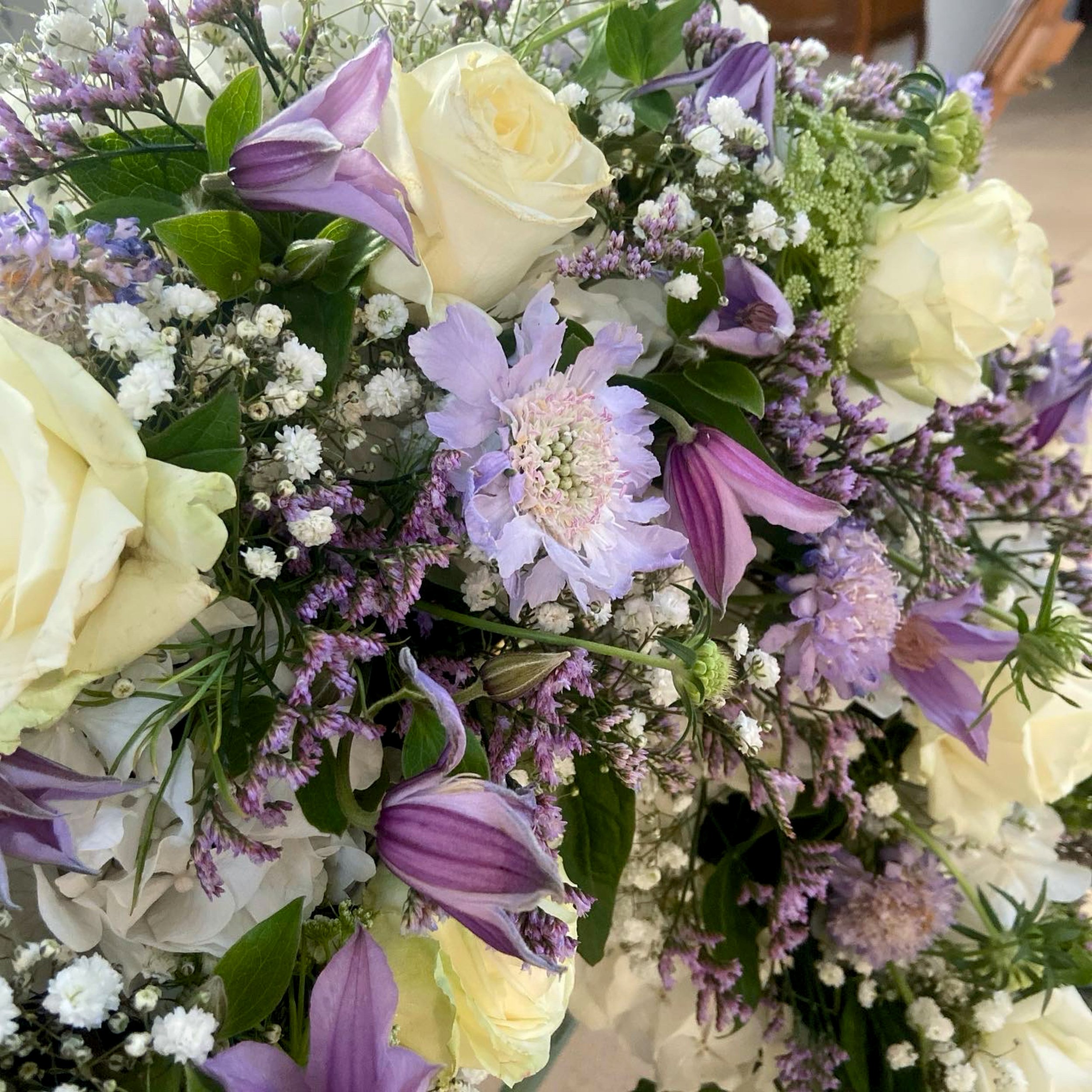 Blumenstrauß mit weißen, lila und violetten Blumen, darunter Rosen, Lilien und Kleeblüten, mit grünen Blättern.