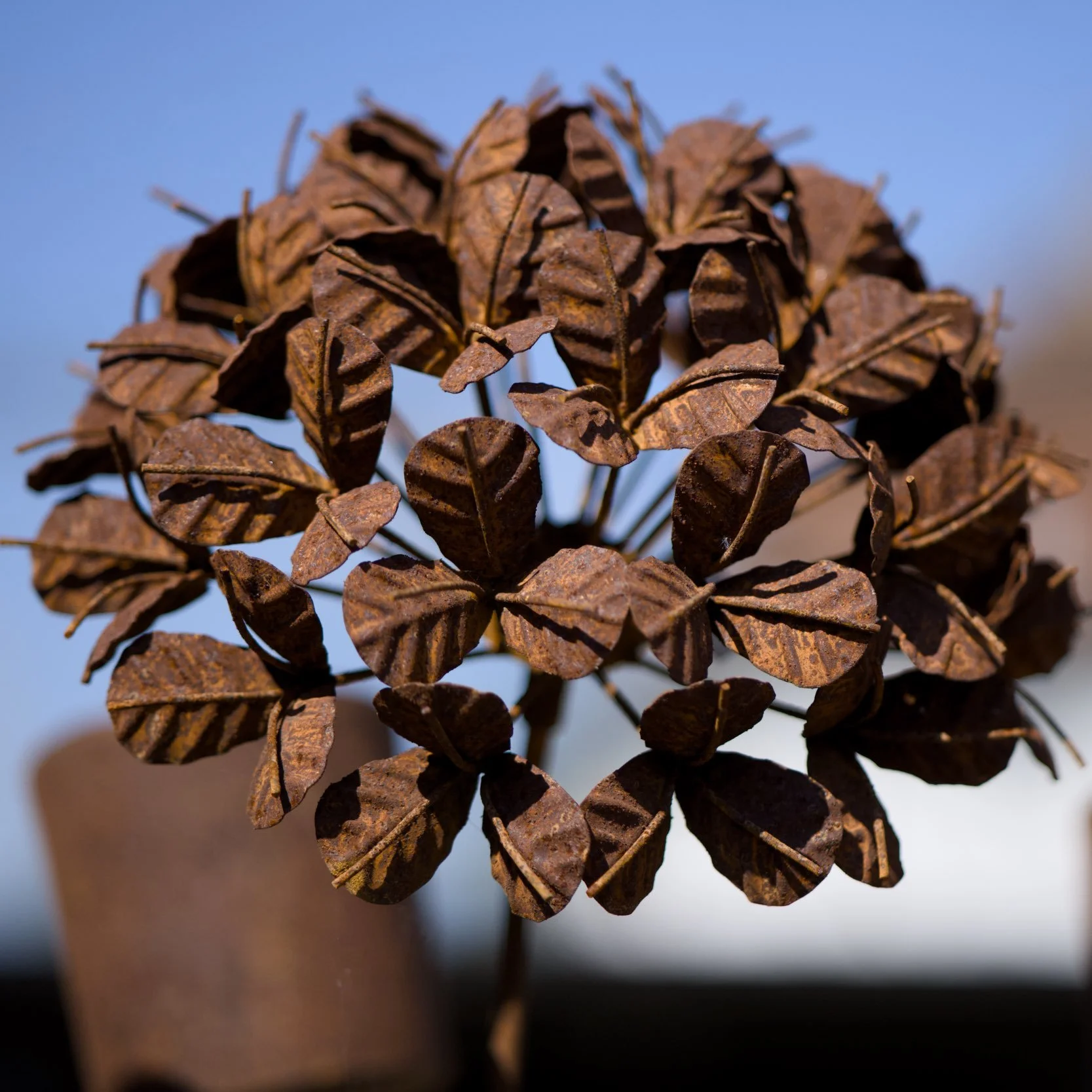 Nahaufnahme eines Dekorationsobjekts aus getrockneten, braunen Blättern, die wie eine Blume angeordnet sind, vor einem unscharfen Hintergrund.