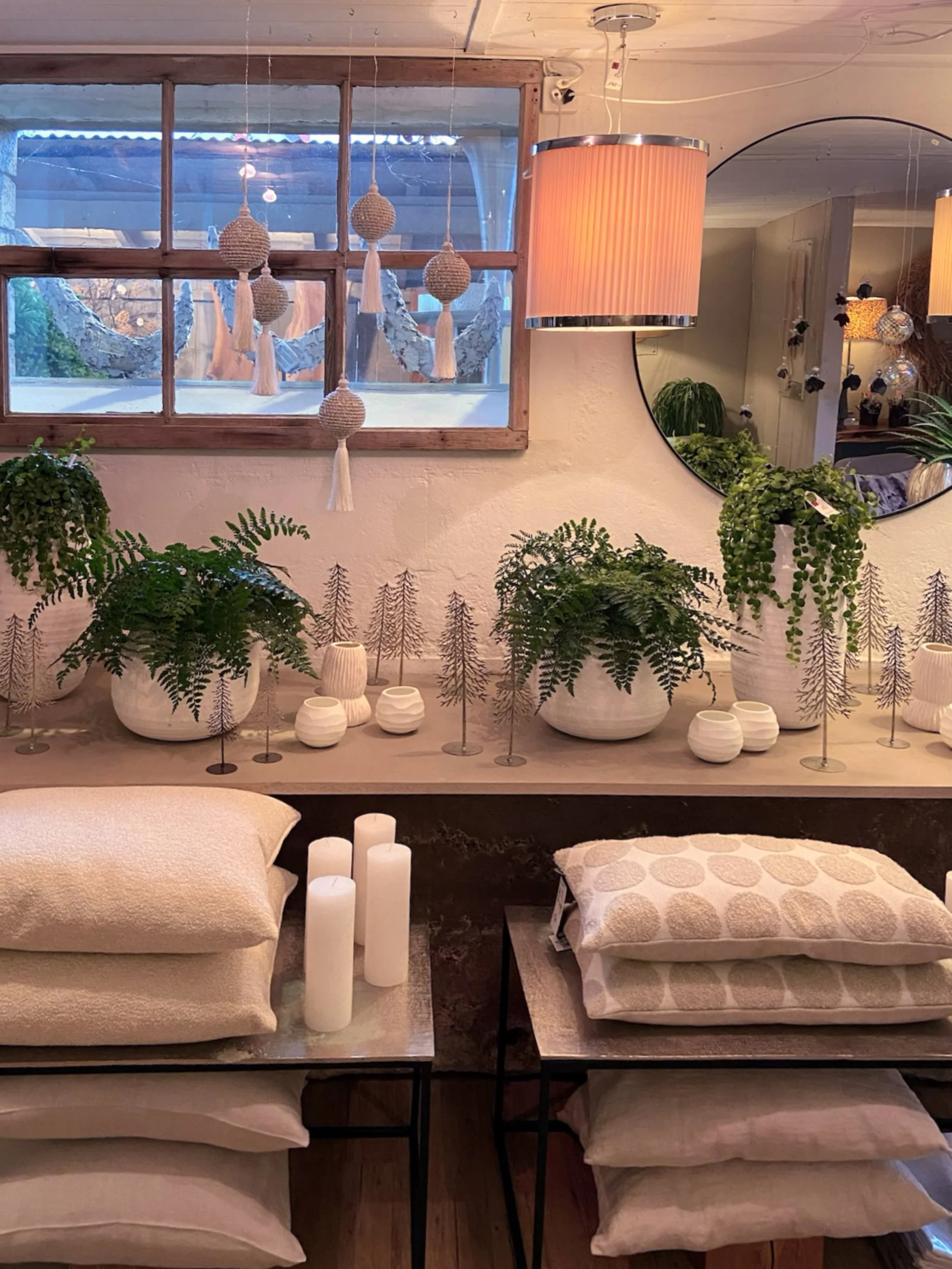 Ein Zimmer mit mehreren weißen Kissen, Kerzen und Pflanzen, eine große Wandspiegel und dekorative Geschirre auf einer Holzablage.