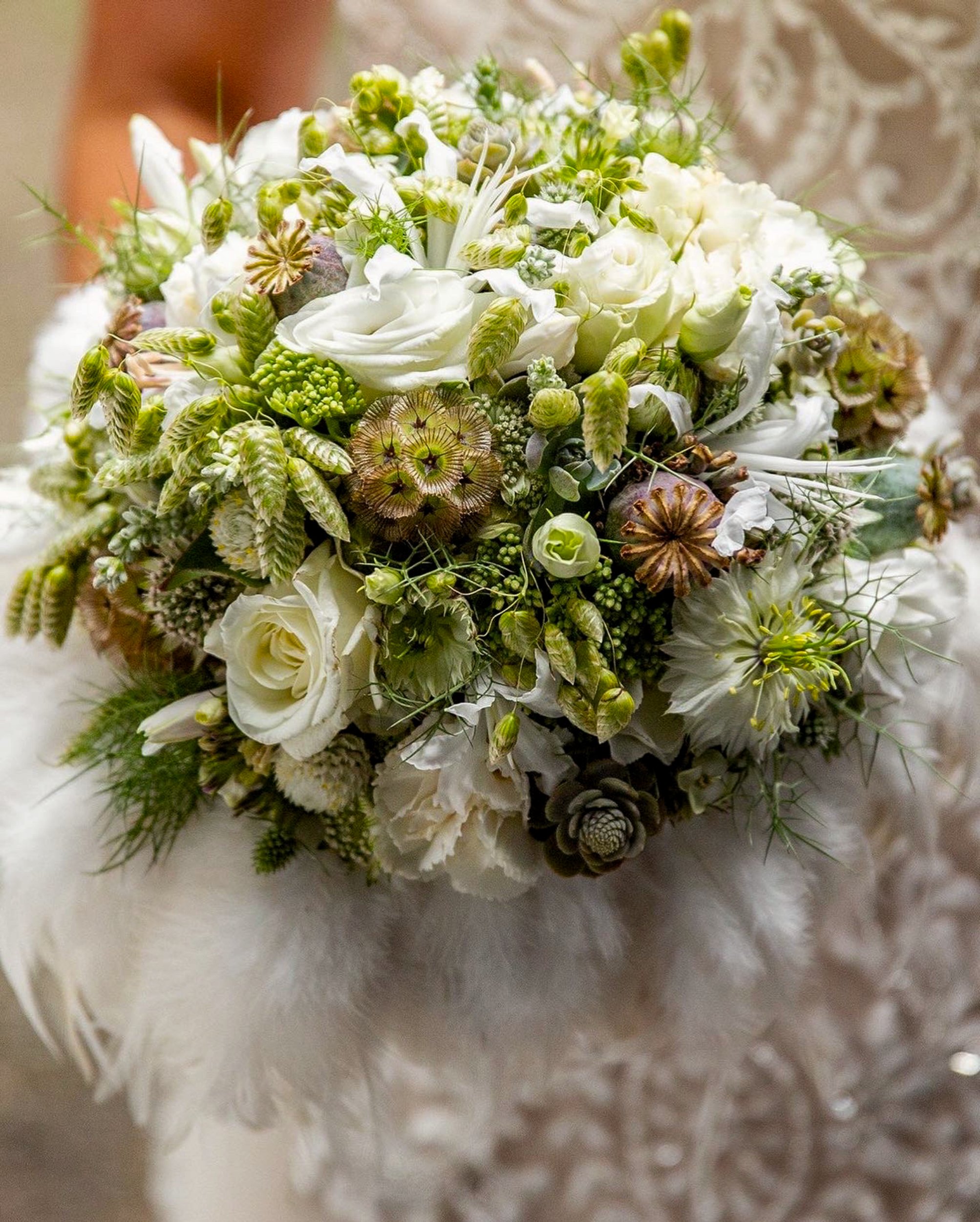 Ein Blumenstrauß mit weißen und grünen Blumen, inklusive weißen Rosen, kleinen weißen Blüten und grünen Gräsern, liegt auf einem hellen, filzigen Untergrund.
