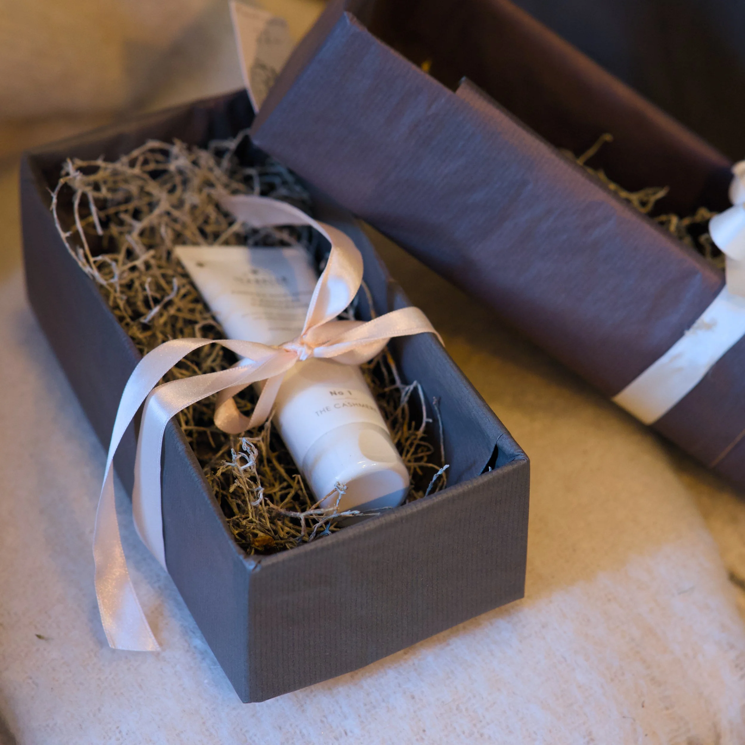 Ein Geschenkpaket in einer Schachtel mit grauem Karton, schwarzem Papier, mit weißem Band und beißendem Papier.