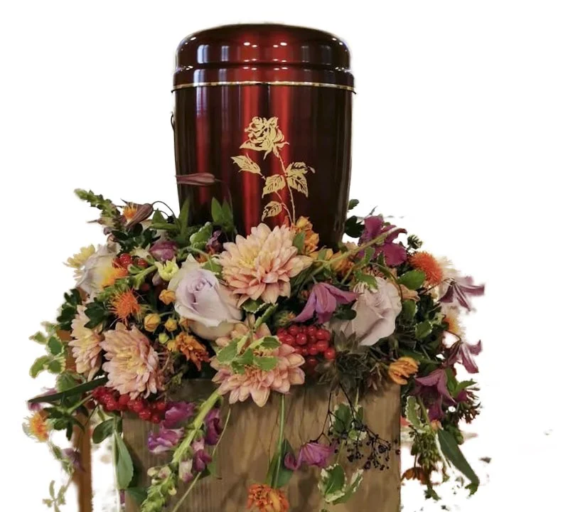 Ein Holzsarg mit goldener Rose auf einem Blumenkranz aus bunten Blumen und Beeren.