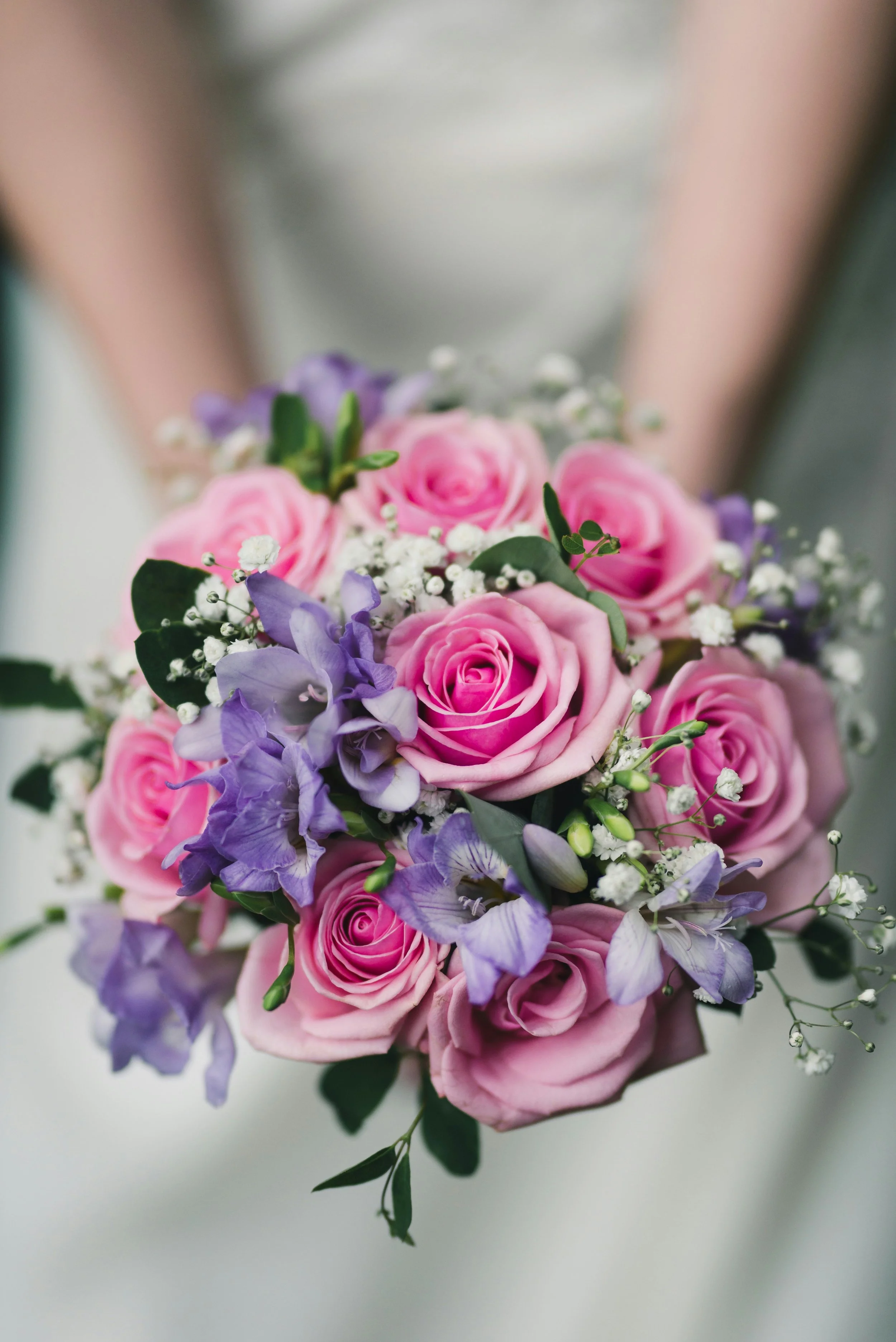 Blumenstrauß mit rosa Rosen, lila Delphiniums, weißen Schleierkraut und grünen Blättern