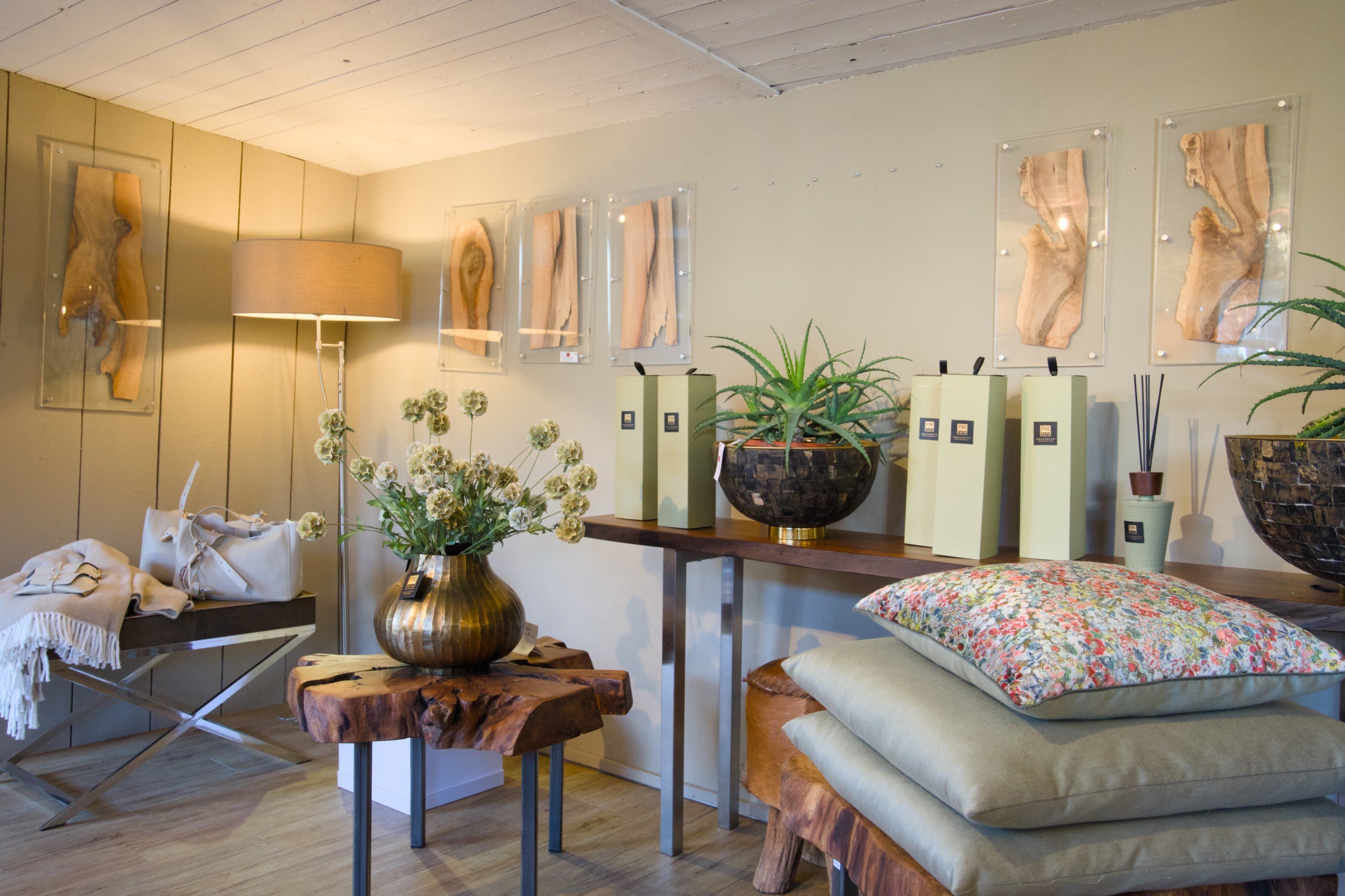 Gemütliches Wohnzimmer mit Holzvertäfelung, Wanddeko aus Holzstücken, Pflanzen, einem Kaffee-Tisch, einem hellen Sofa mit buntem Kissen, Lampen und Dekorationsartikeln.