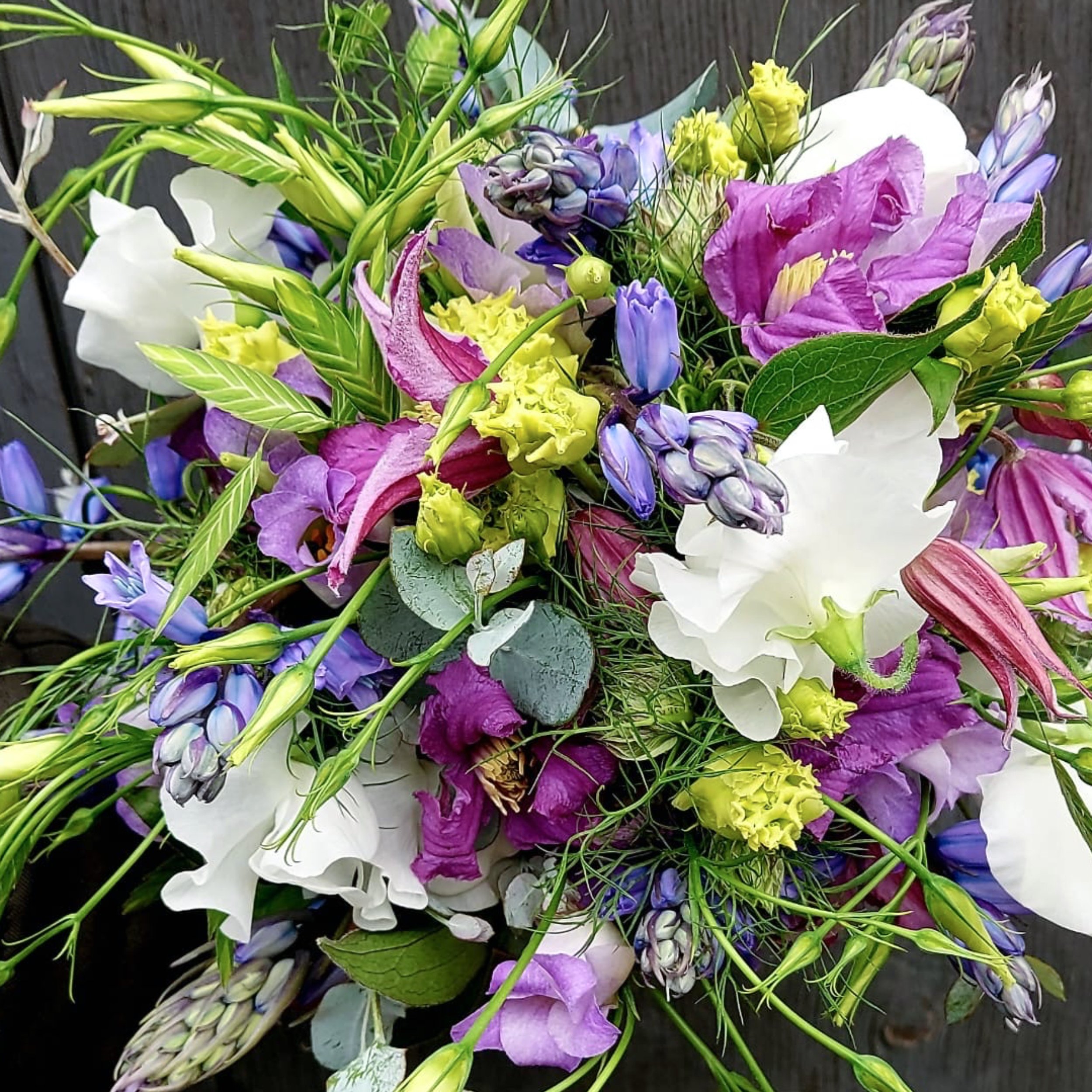Blumengebinde mit weißen, lilafarbenen und gelben Blumen auf dunklem Hintergrund.