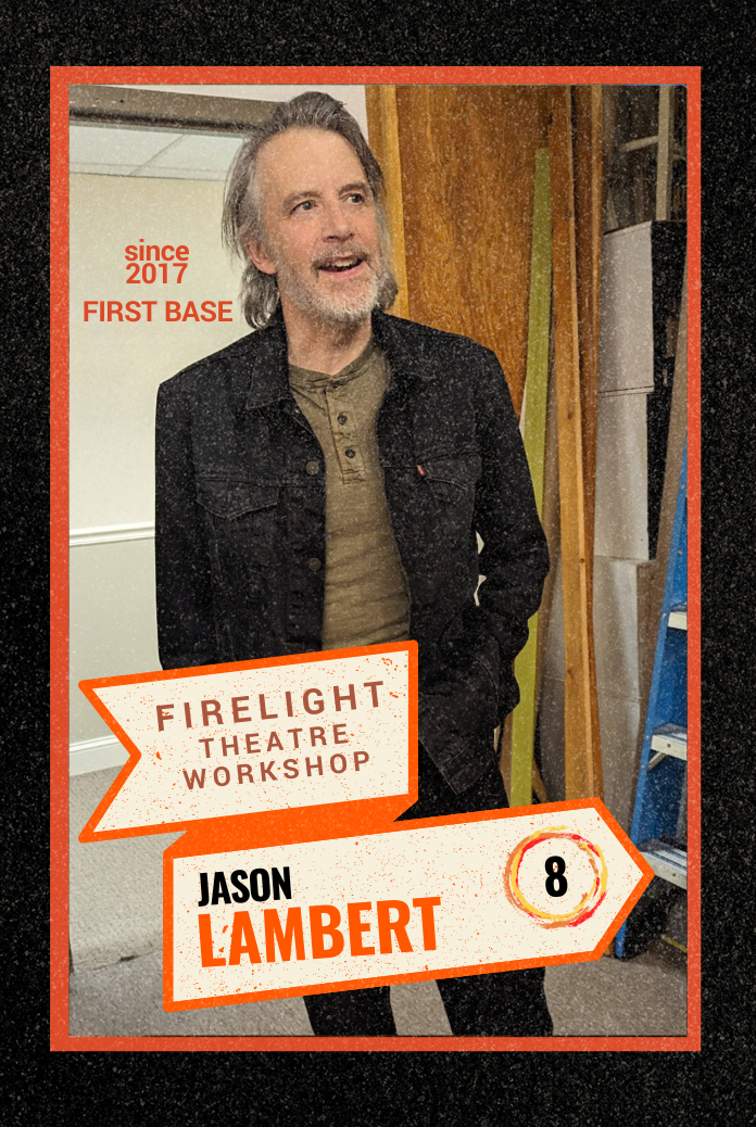 Co-Artistic Director of Firelight, Jason Lambert, wearing a black jacket and a brown shirt, standing indoors in front of a wooden wall and a metal storage shelf.