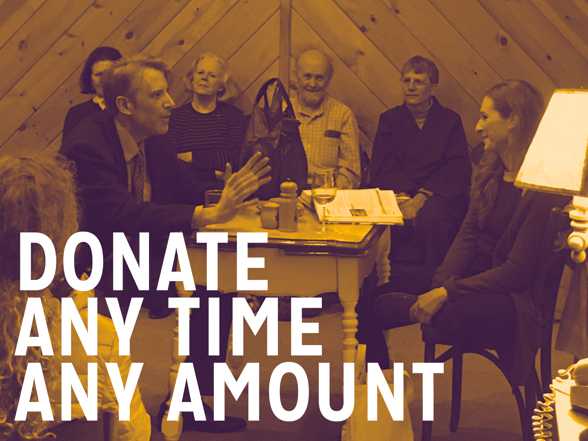 A group of eight people sitting around a table in a wooden-paneled room, engaged in a discussion, with the text 'Donate Any Time Any Amount' overlaid on the image.