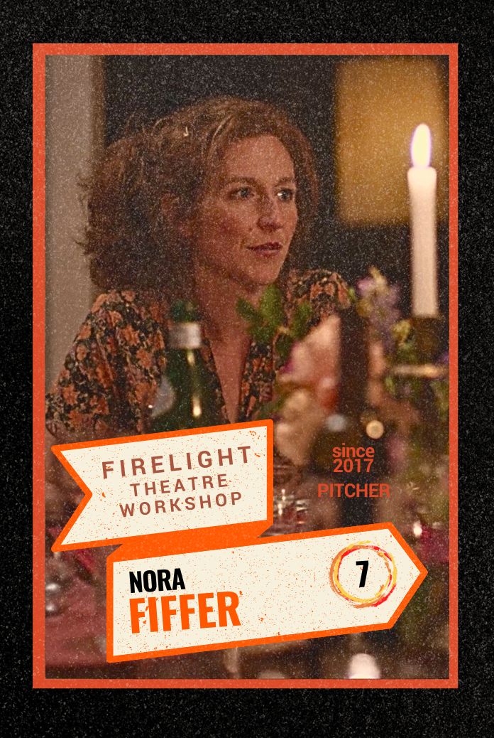 Co-Artistic DIrector of Firelight, Nora Fiffer, at a dinner table with a lit candle, flowers, and bottles in front of her. A still from the Firelight film, Dinner Time. 