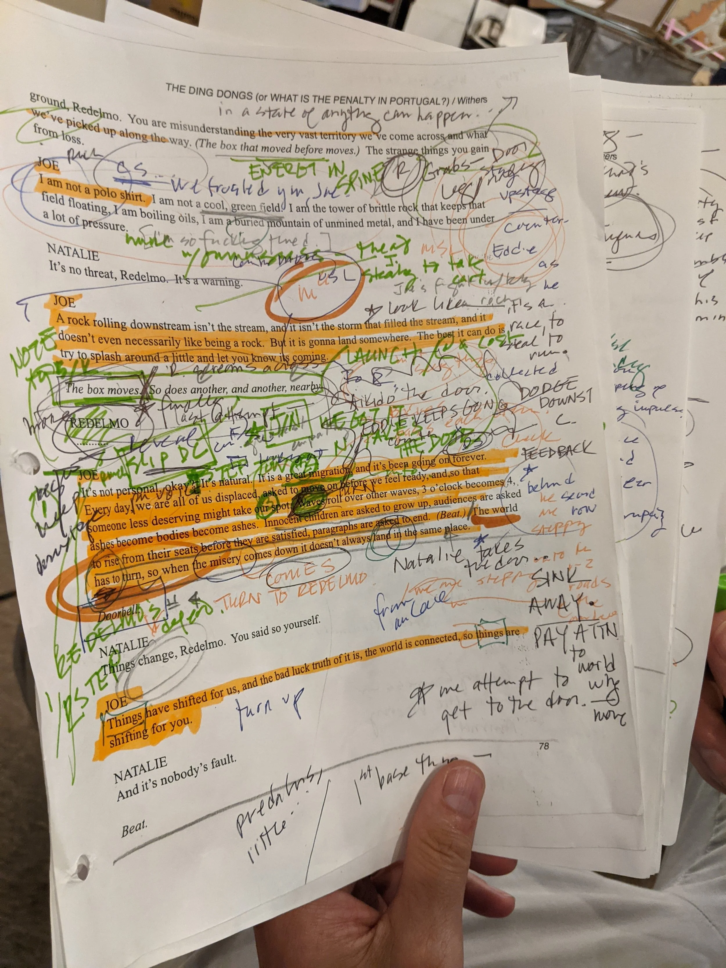 Close-up of a script page filled with markings, highlighted text, and handwritten notes in various colors. The page contains a printed excerpt with orange highlights and handwritten annotations in green, blue, purple, orange, and black ink.