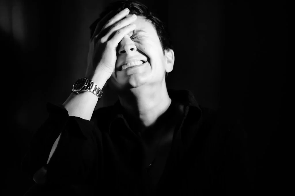 Uomo sorridente coprendosi il viso con una mano in una foto in bianco e nero.