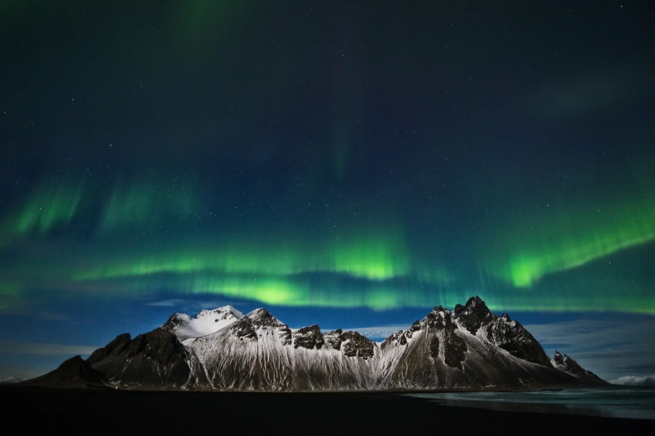 Montagne innevate sotto le luci dell'Aurora boreale nel cielo notturno