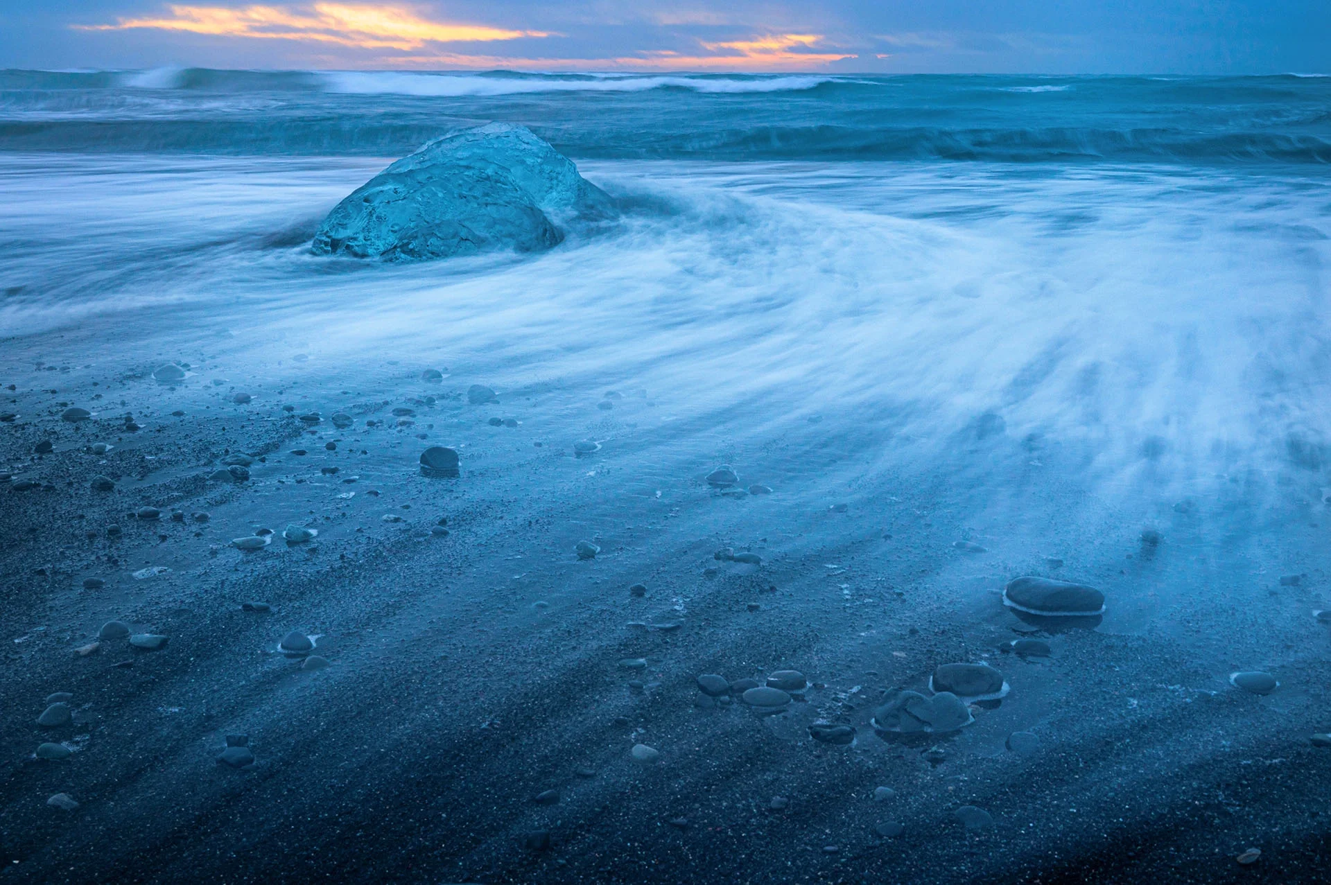 Sabbia e ciottoli sulla spiaggia con mare in movimento e cielo al tramonto.