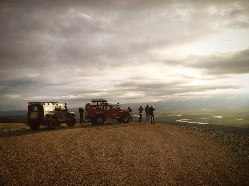 Tre veicoli fuoristrada parcheggiati su una collina, con alcune persone che guardano il paesaggio sotto un cielo nuvoloso.