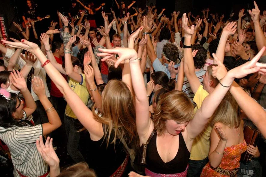 Crowd of people dancing with raised hands at a lively party or concert.