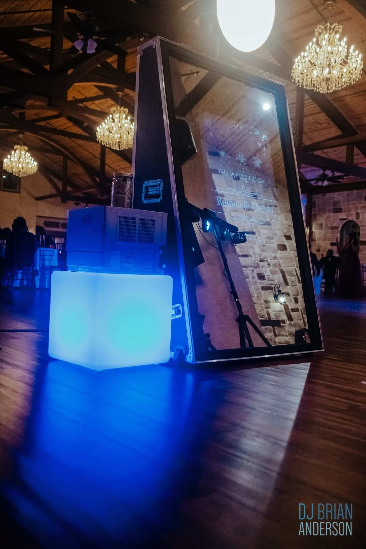 Photo of a wedding signboard on the floor at an indoor reception with chandeliers and guests in the background. The sign reads "The Wedding of Regina & Lewis."