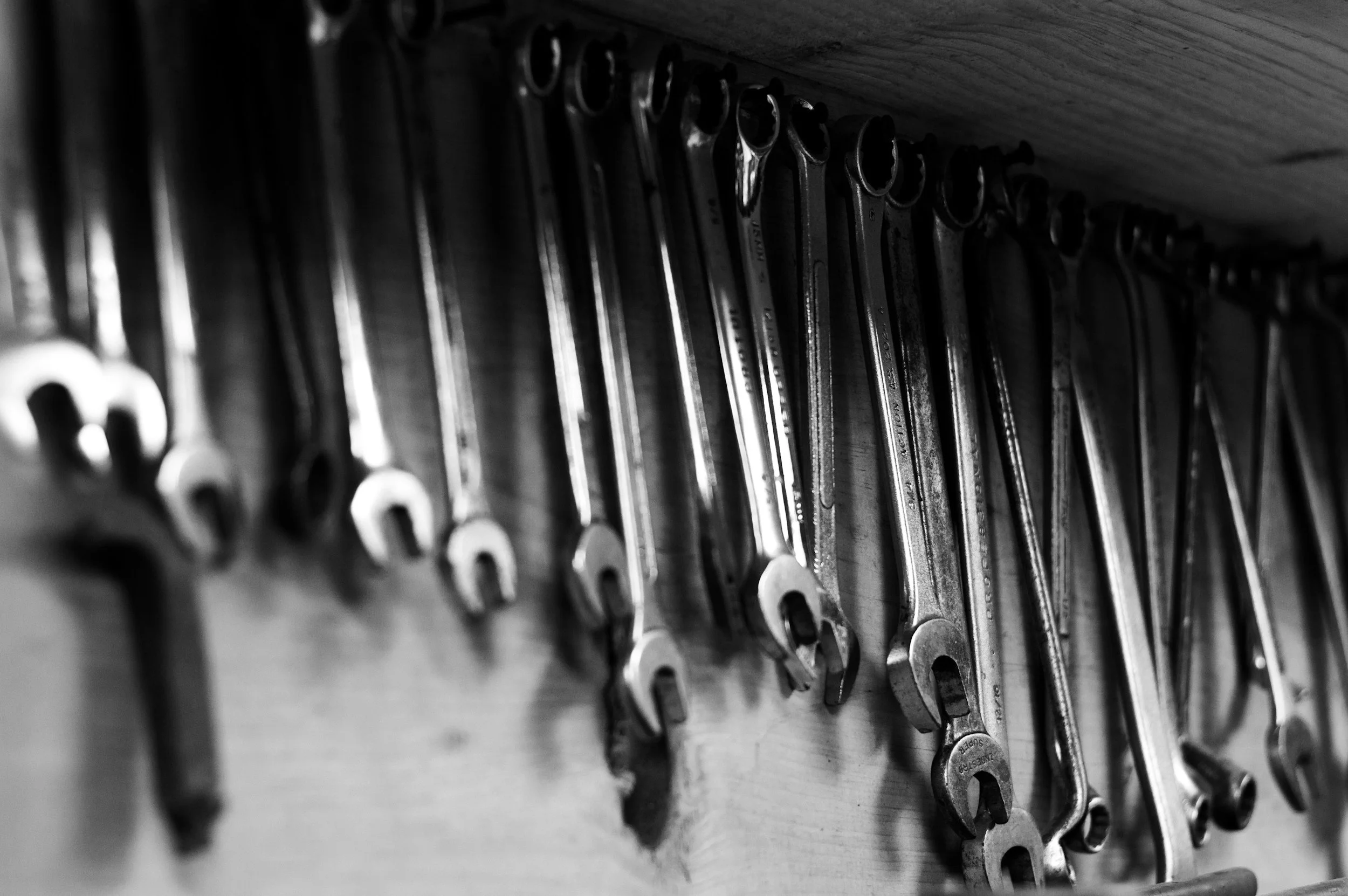 Black and white photo of a row of open-end wrenches hanging on a wooden wall or shelf.