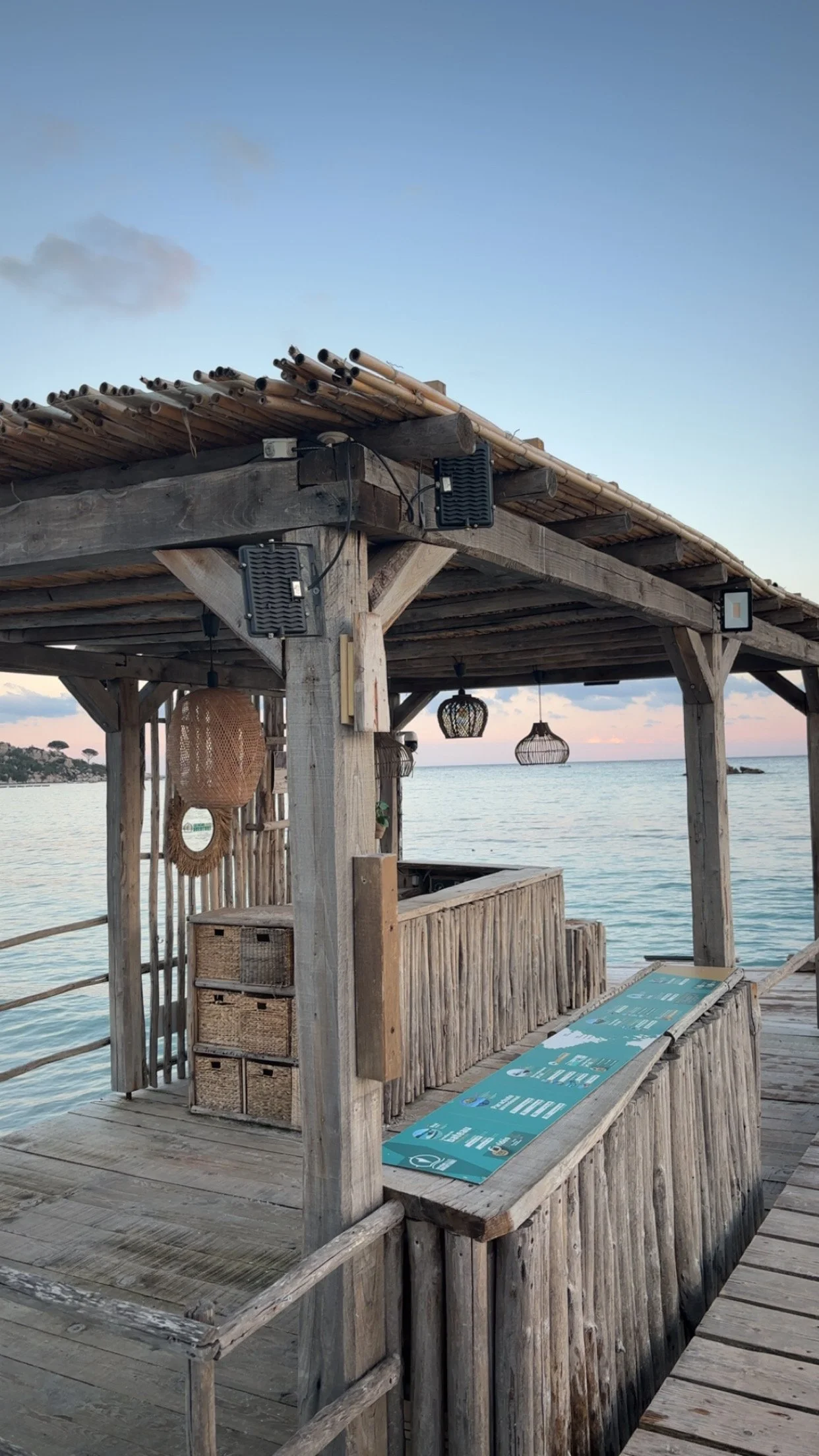 Bar en bois en bord de mer avec des lampes suspendues et un tableau avec un menu.