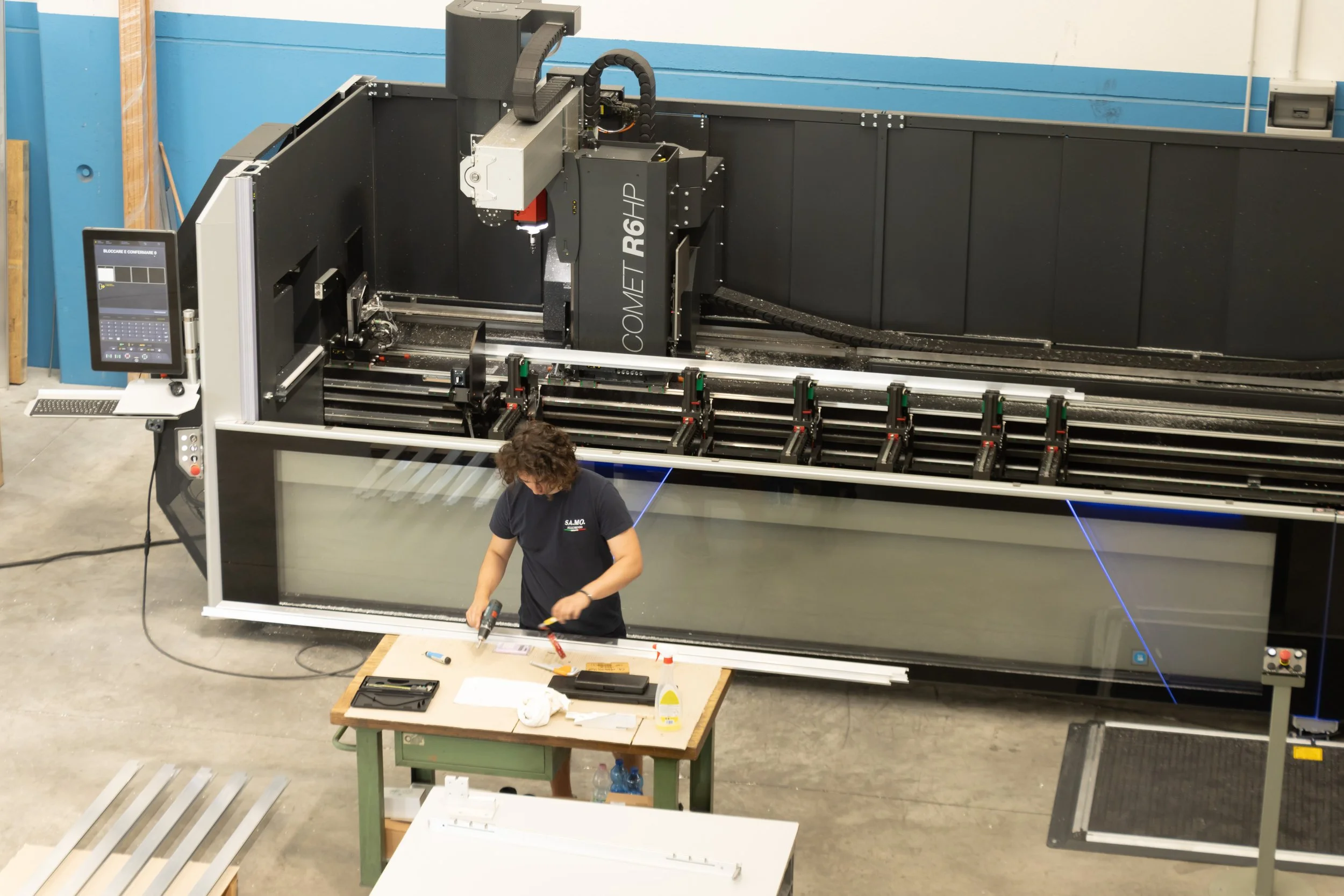 Un operatore lavora vicino a una grande macchina industriale con laser in un laboratorio o fabbrica, mentre monta o ripara parti di una grande struttura in metallo.