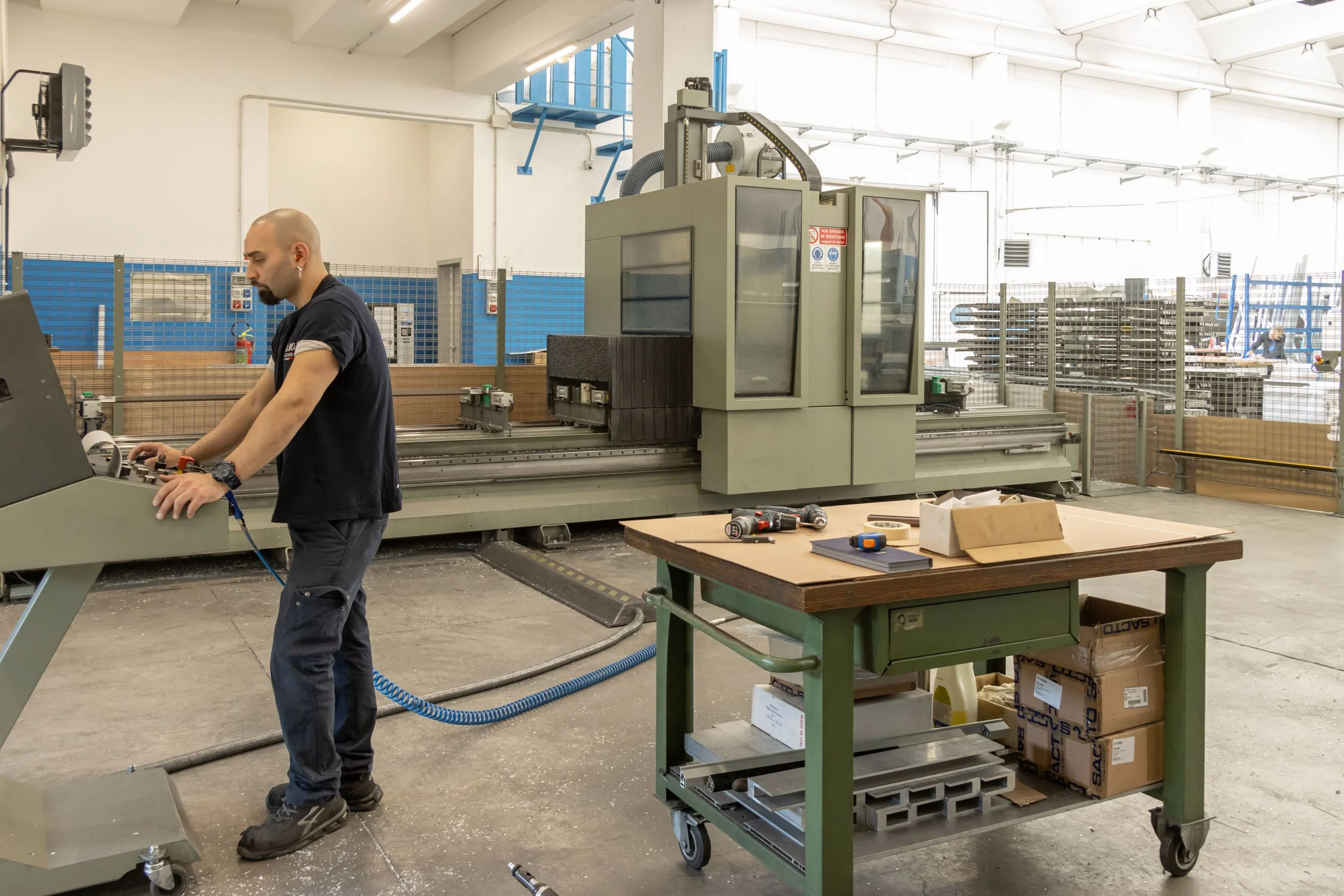 Un uomo in officina mentre lavora con una macchina CNC in un ambiente industriale spazioso e ben illuminato.