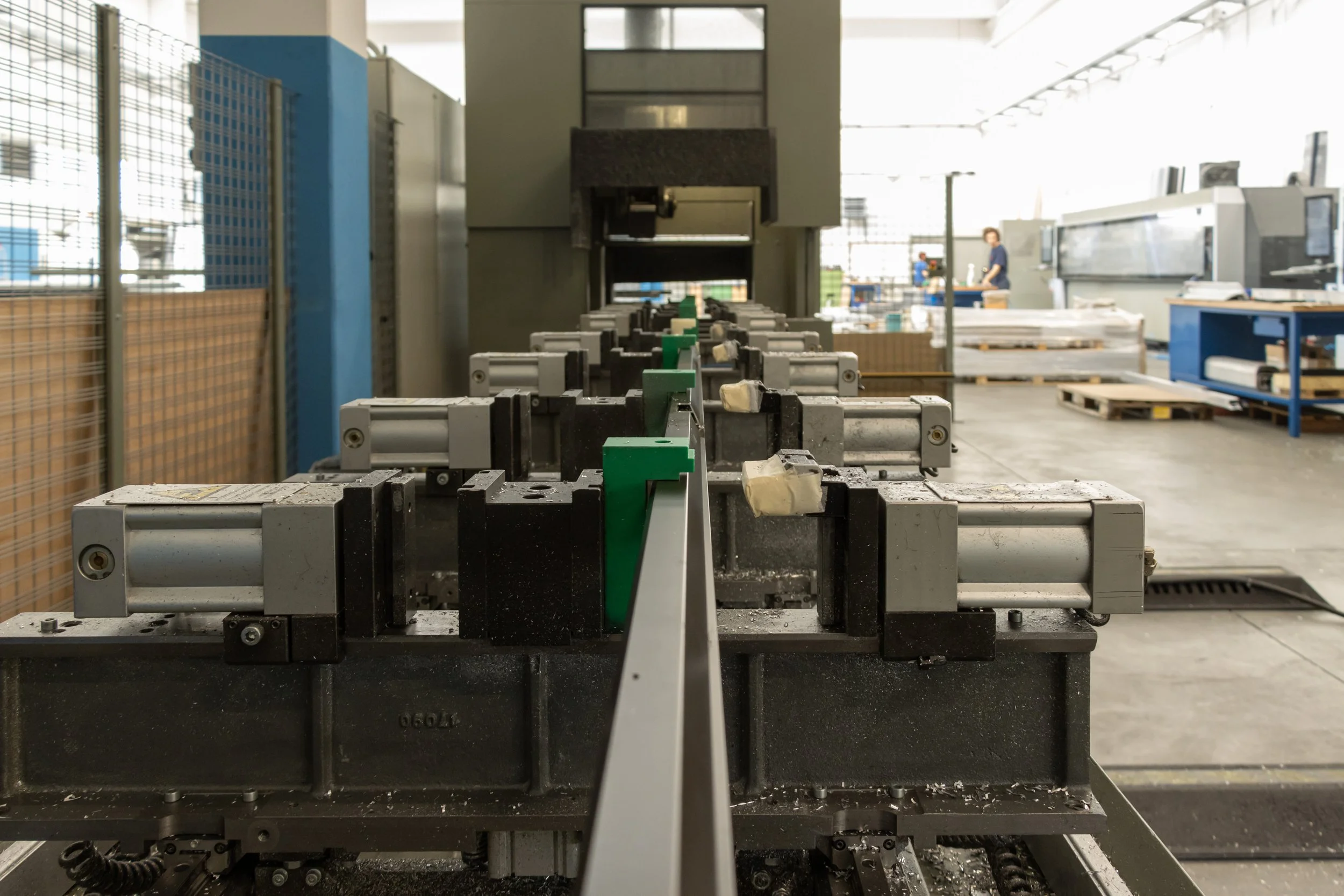 Immagine di un'industria con macchinari per la produzione o il montaggio di componenti metallici in un ambiente di fabbrica, con una persona al sfondo.
