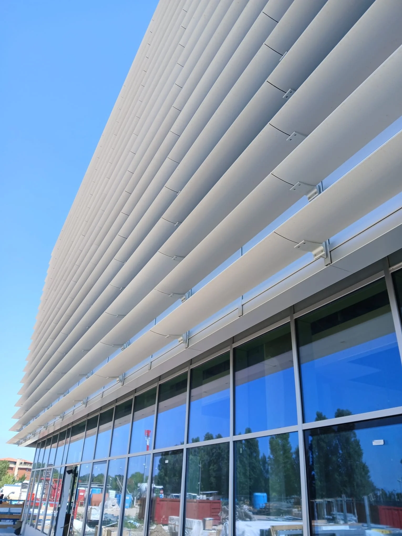 Edificio moderno con facciata di vetro e persiane bianche orizzontali.