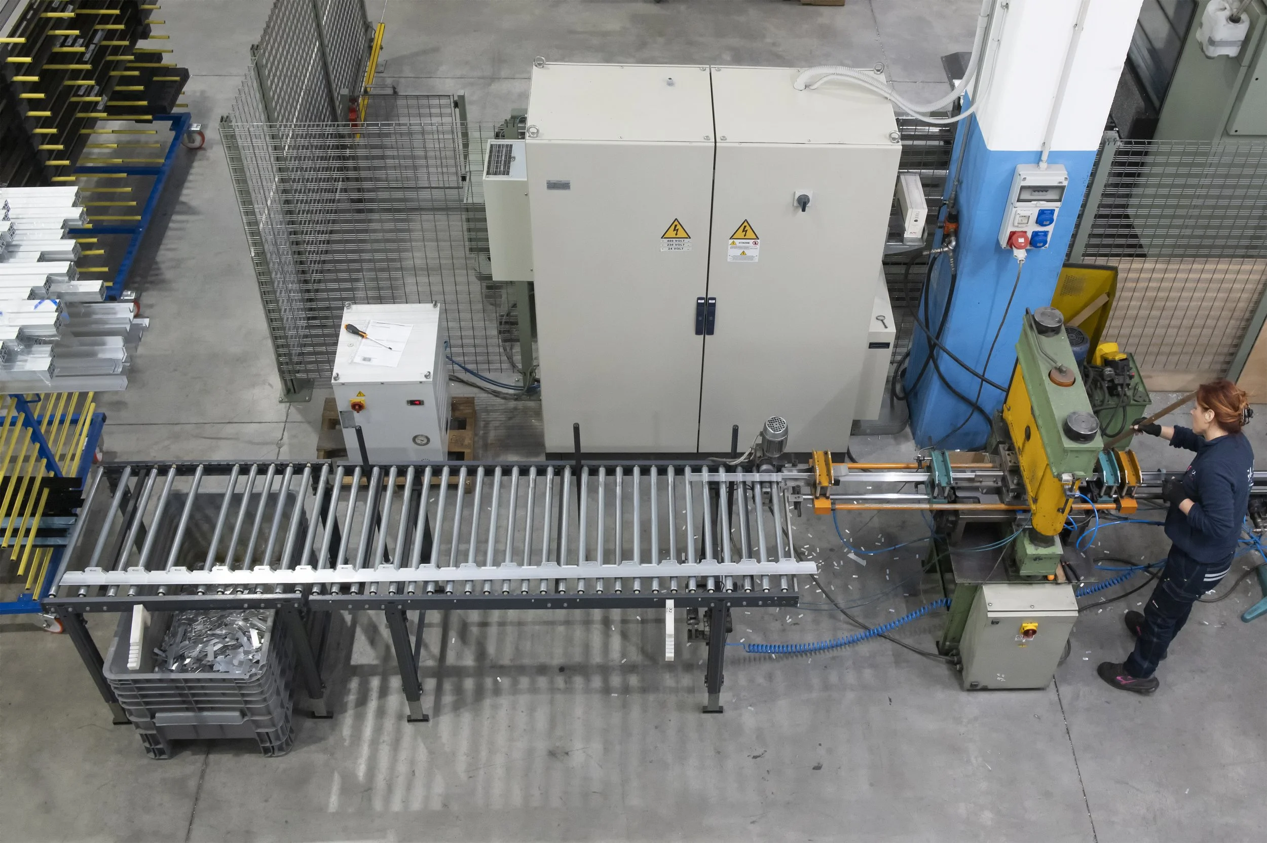 Un operatore sta utilizzando una macchina industriale all'interno di un magazzino o fabbrica, con scaffali di metallo e vari strumenti.