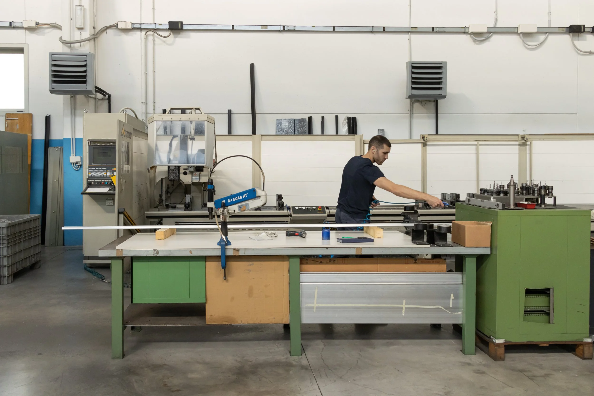 Un uomo lavora su una macchina industriale in un'officina, circondato da attrezzi e strumenti.