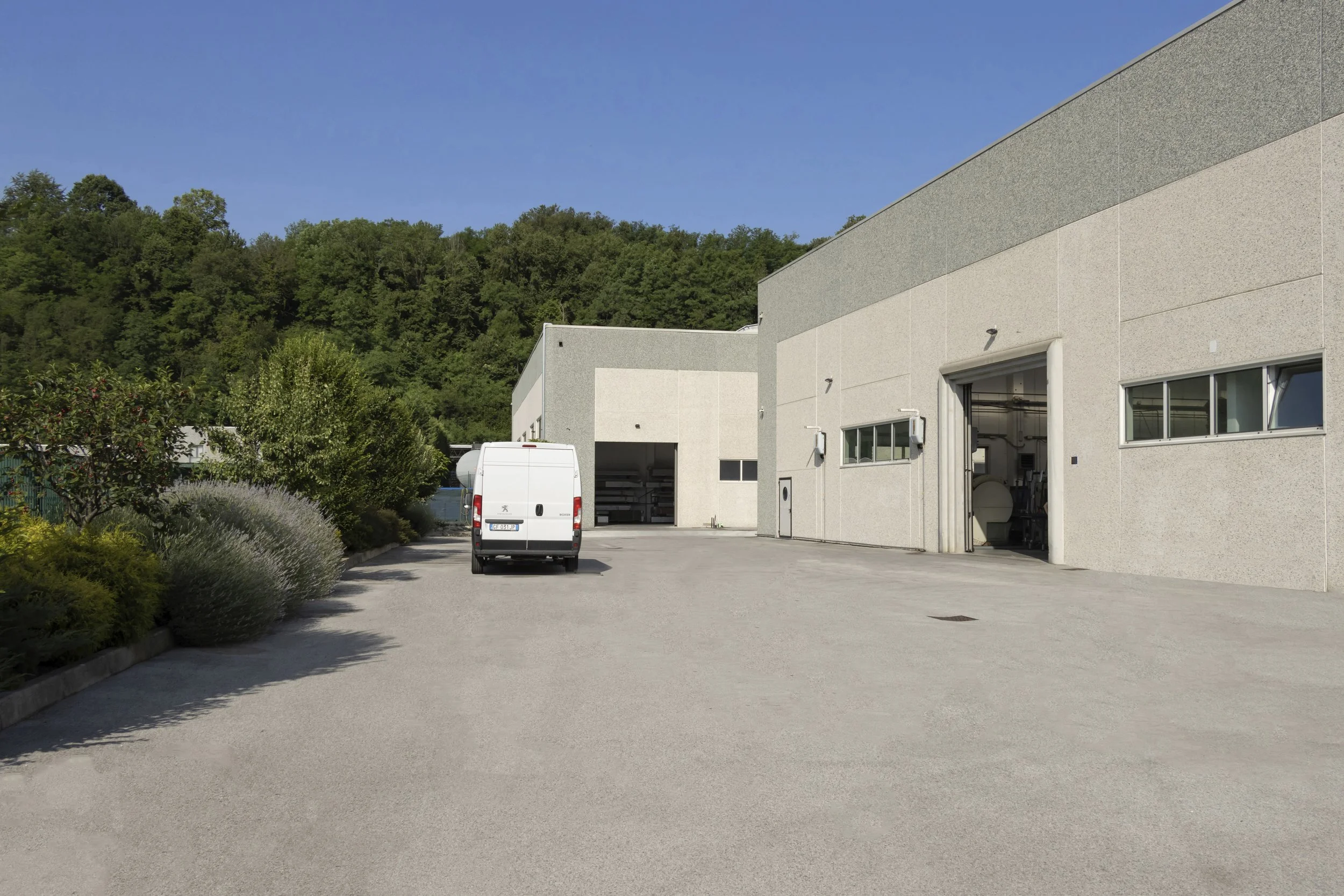 Depo industriale con camion e edifici in stile moderno, con fondale di colline verdi e cielo sereno.