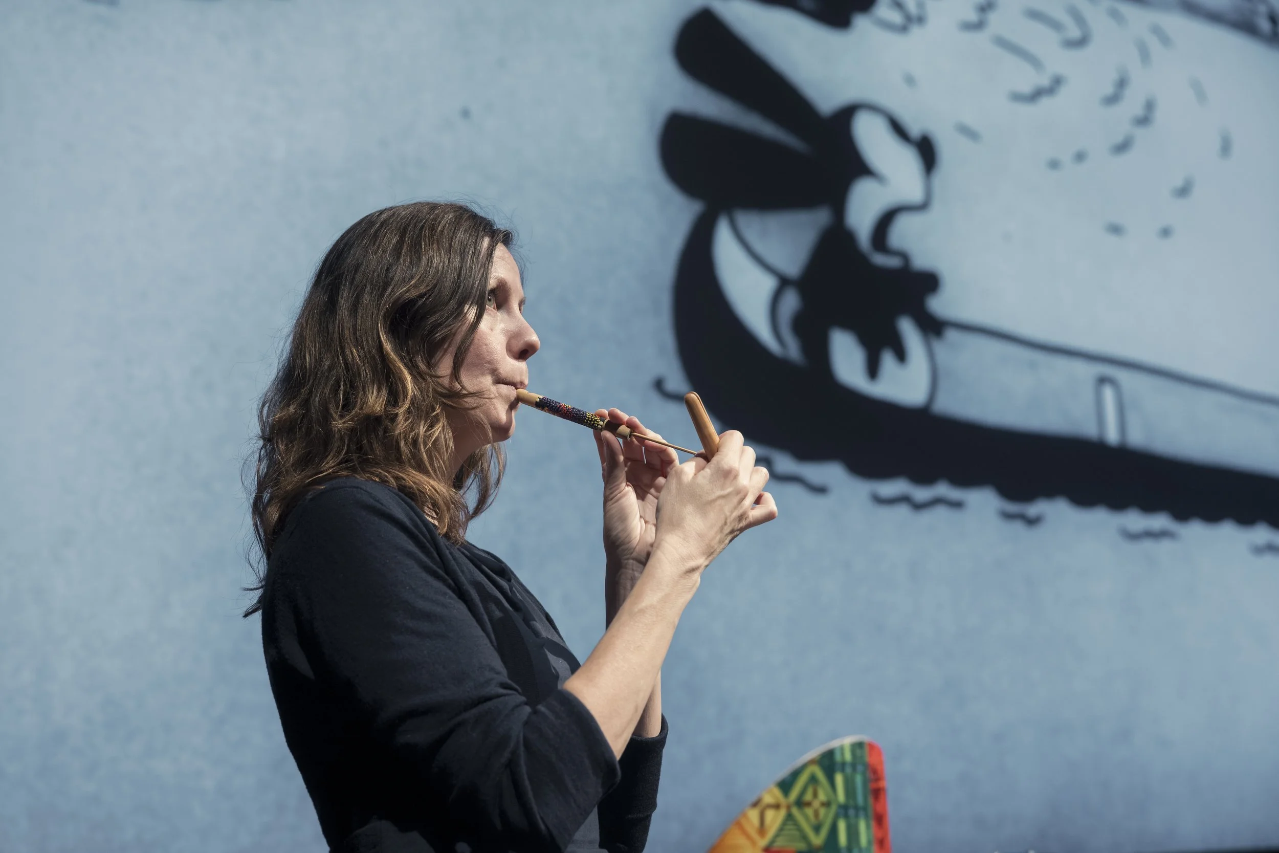 Kvinne som spiller på et didgeridooinstrument med en stor skygge av en aboriginsk kunst på veggen bak henne.