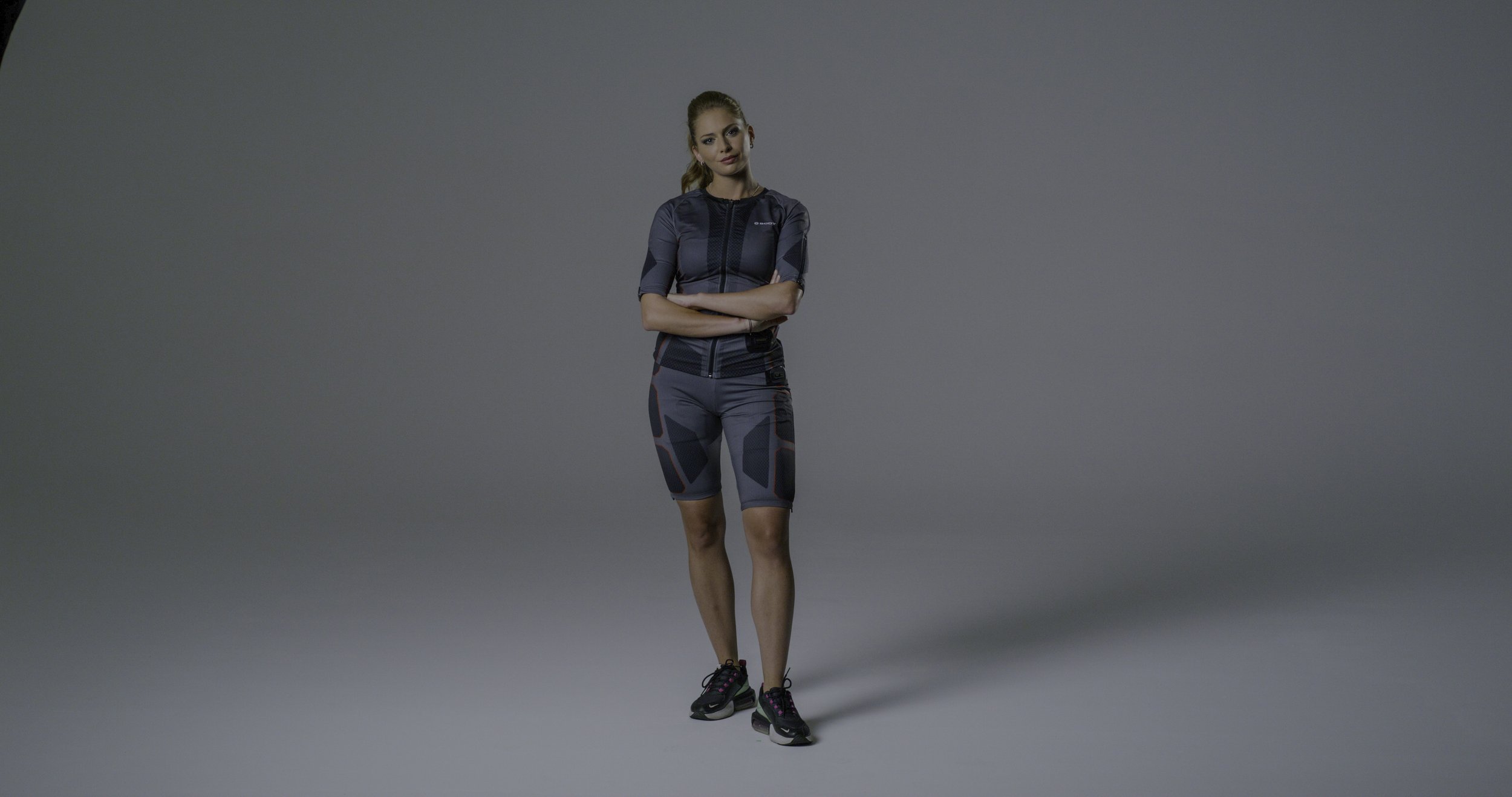 A woman in athletic wear standing with arms crossed against a plain gray background.