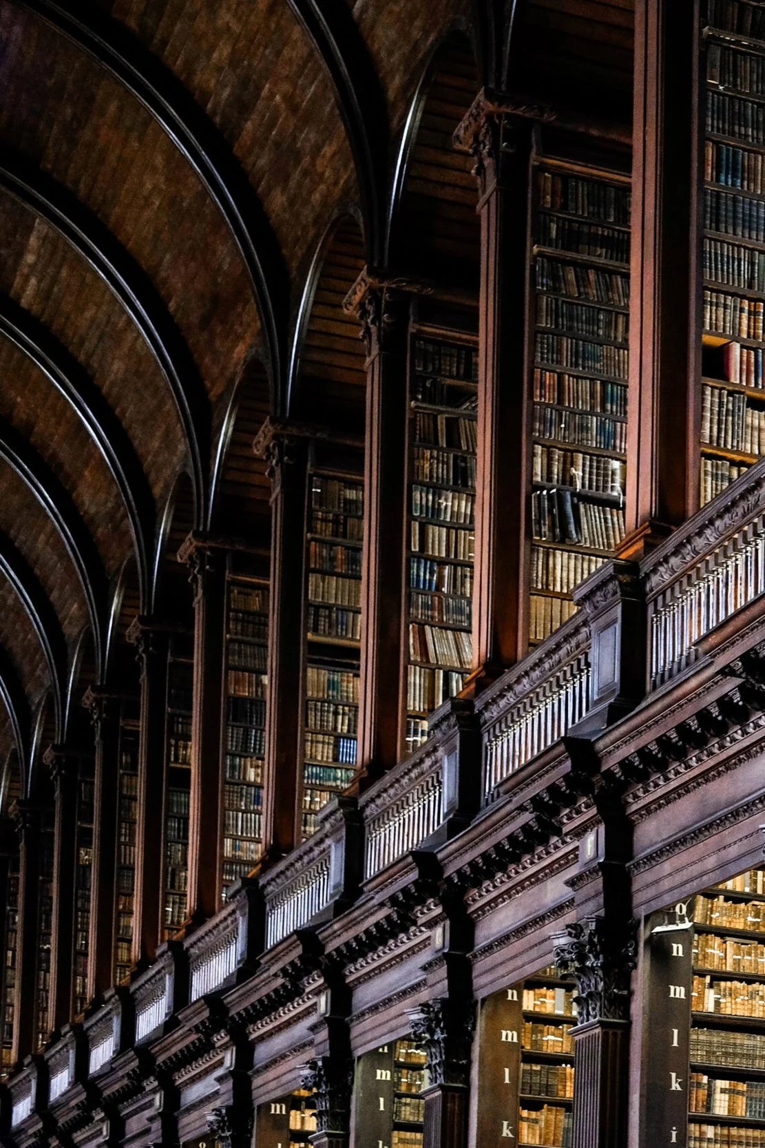 Interior of an old, large library with tall wooden bookshelves filled with books, ornate woodwork, and arched ceiling.
