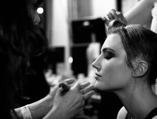 A woman getting her makeup done by a makeup artist in a salon.