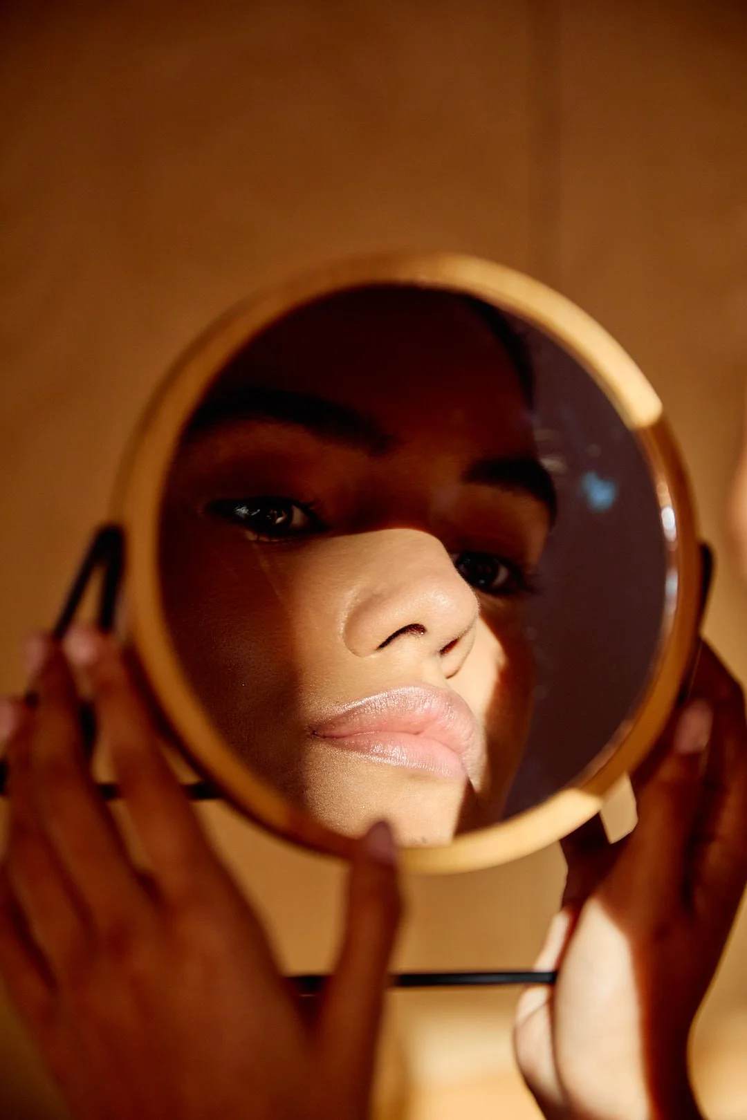 Natural Glow service, showcasing a close-up of a woman's face reflected in a small round mirror, showing her eyes, nose, and lips.