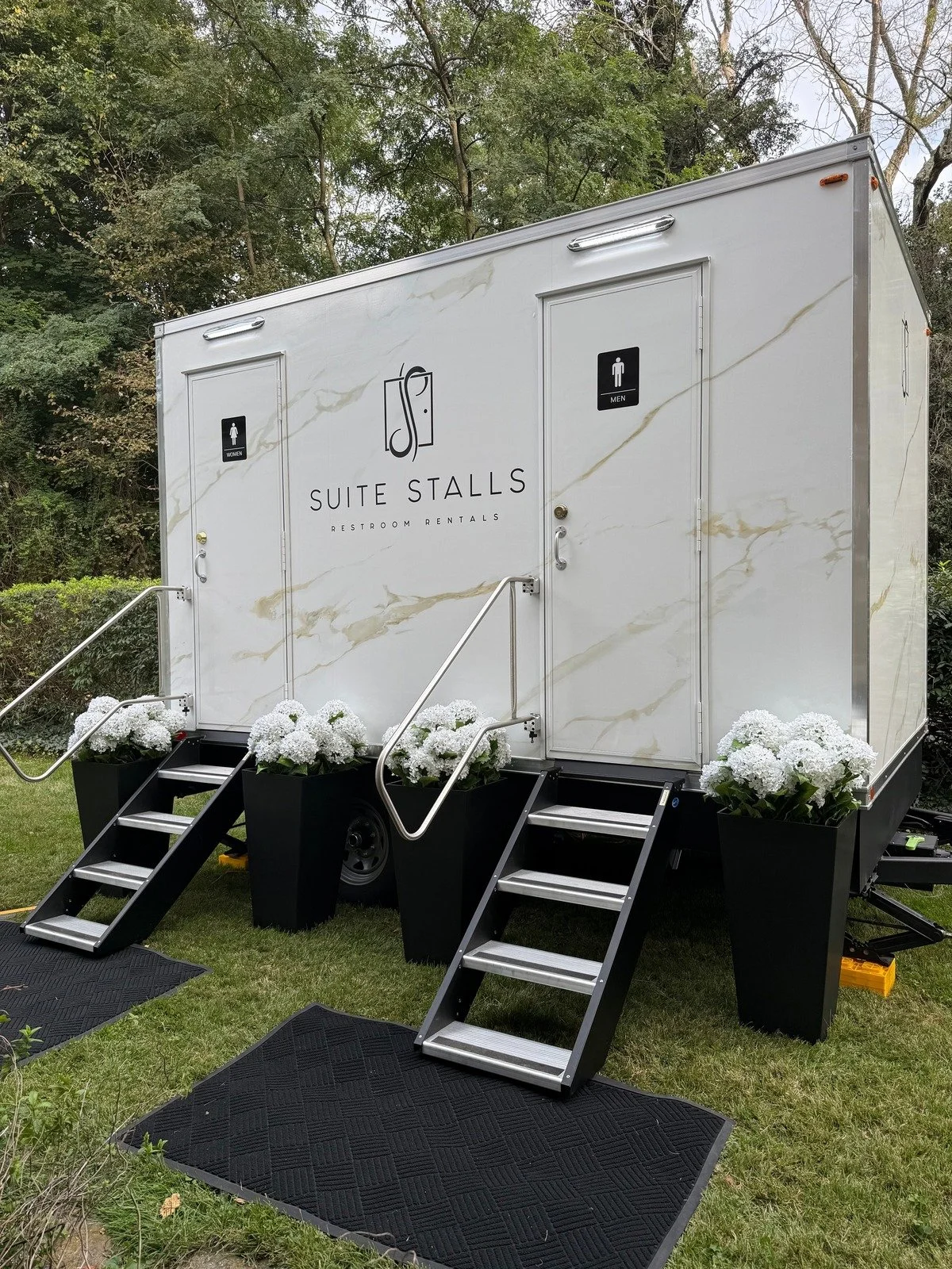 Angled view of the Suite Stalls restroom trailer with white wedding flowers and guest entrance steps.